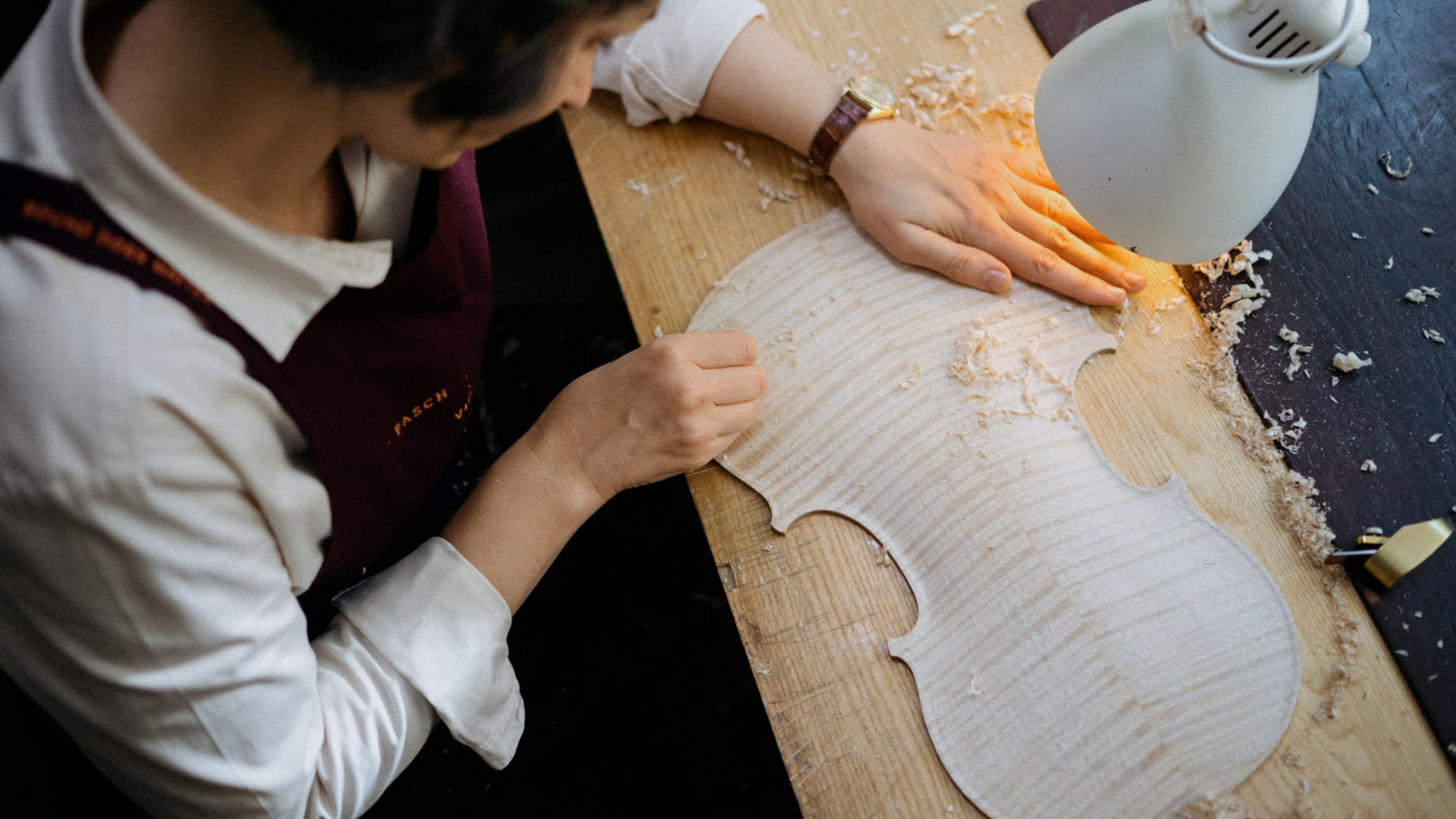 Violin maker shaping a violin top among wood shavings.