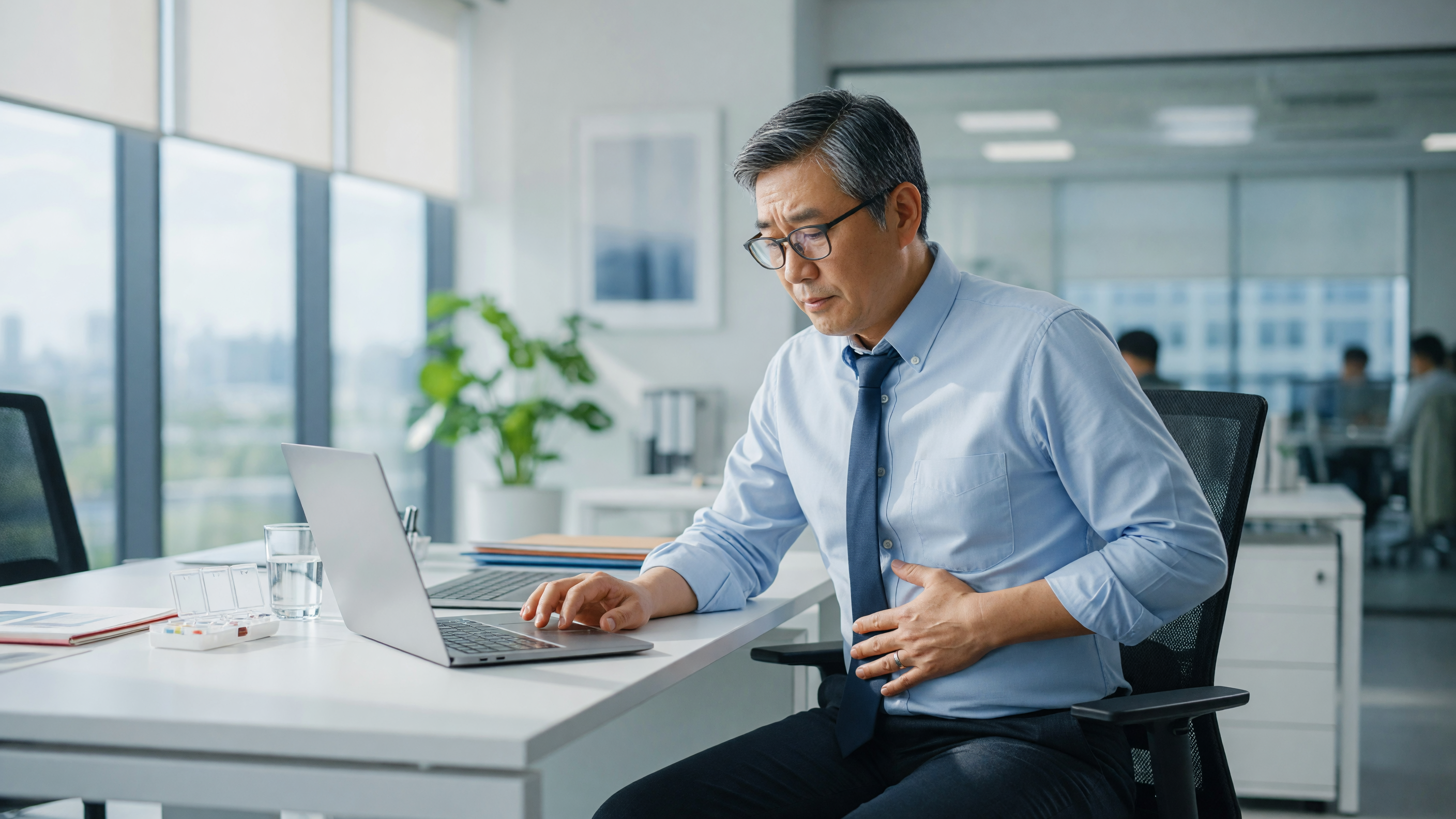 Office worker holding abdomen at desk illustrating hernia risk factors from sitting all day