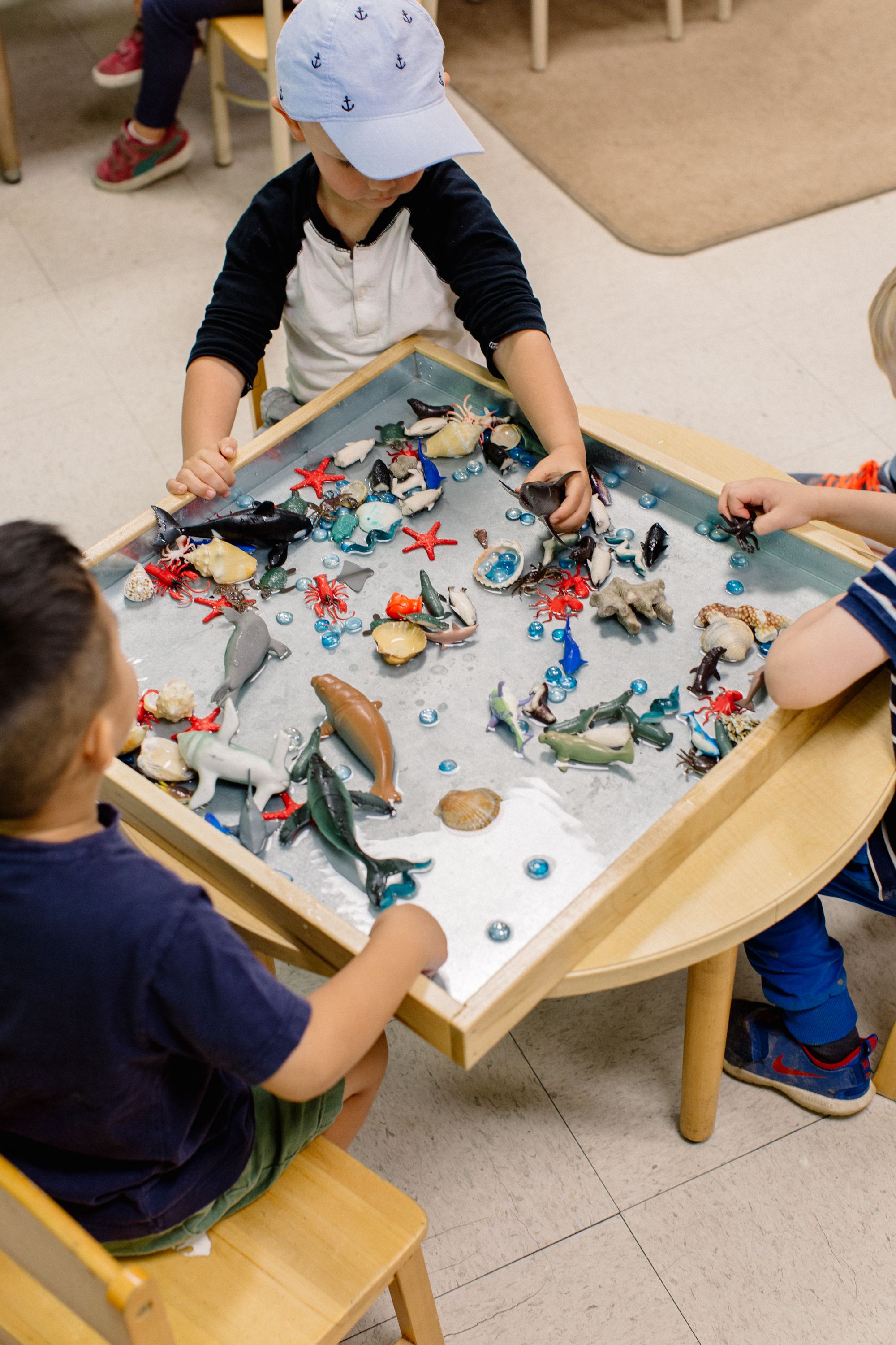 Three young children play with ocean figurines in a tray of water.