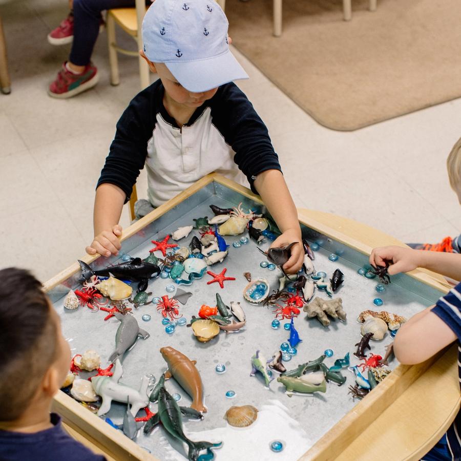 Three young children play with ocean figurines in a tray of water.