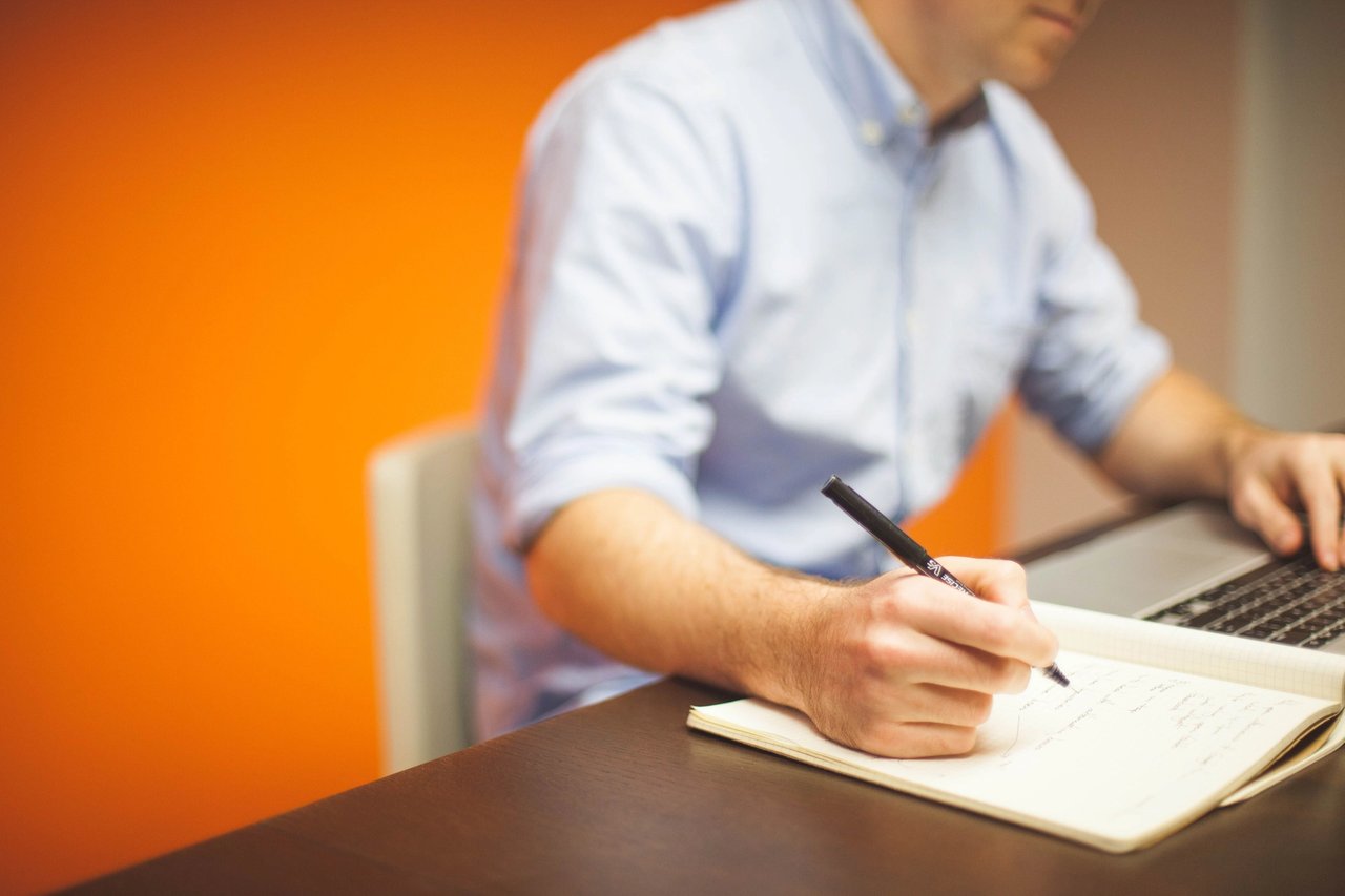 Man sitting at laptop in an orange room, taking notes.