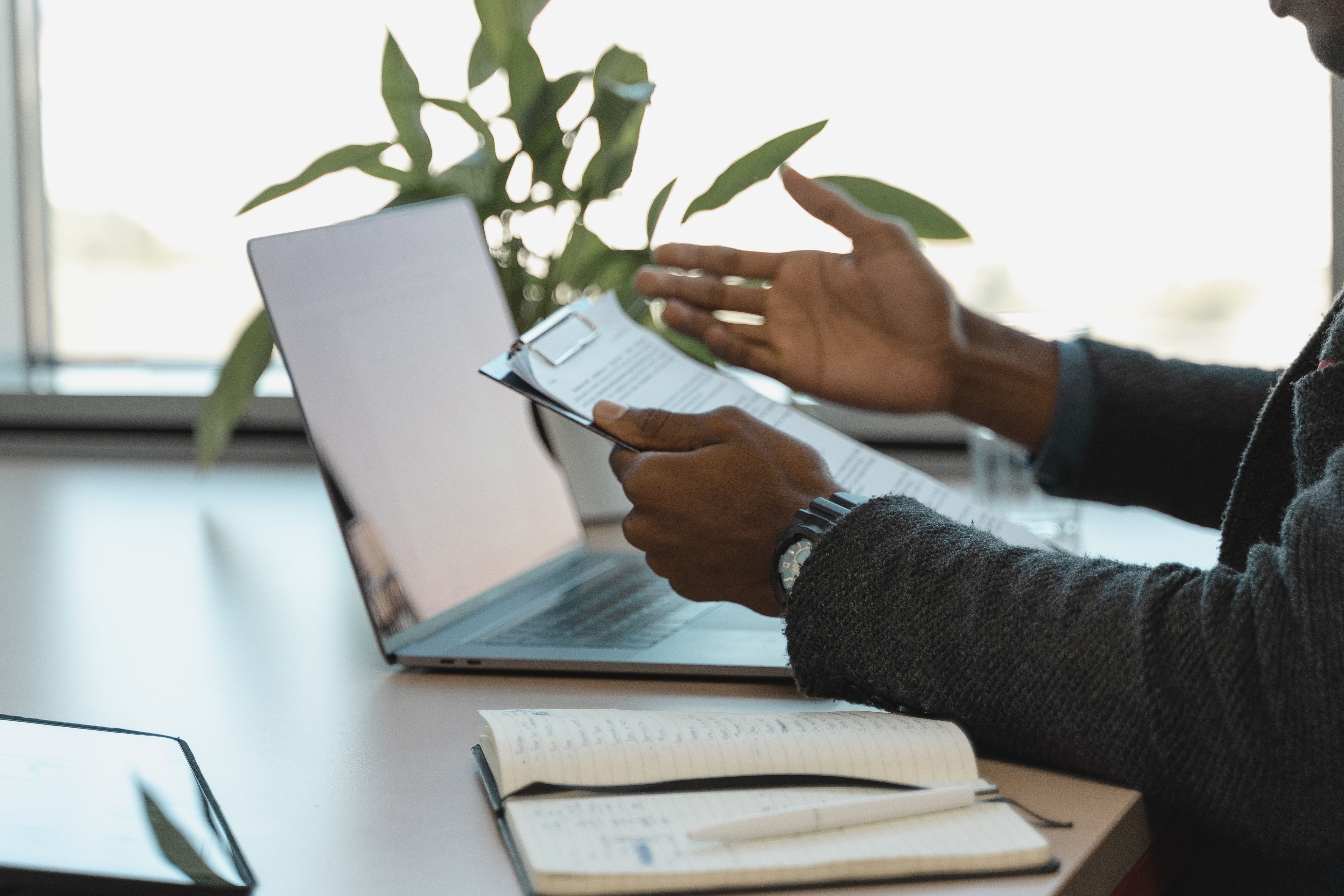 Job seeker sat at laptop confused while studying a printed job description.