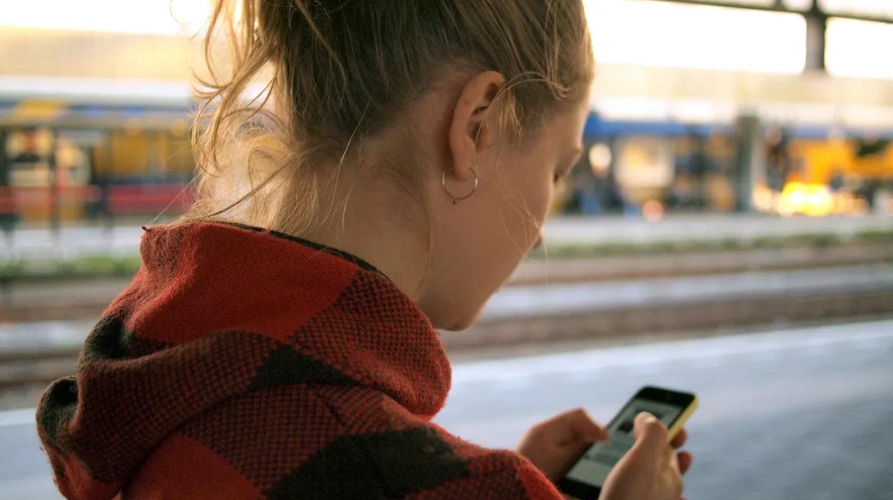 A girl at a train station using her phone. 
