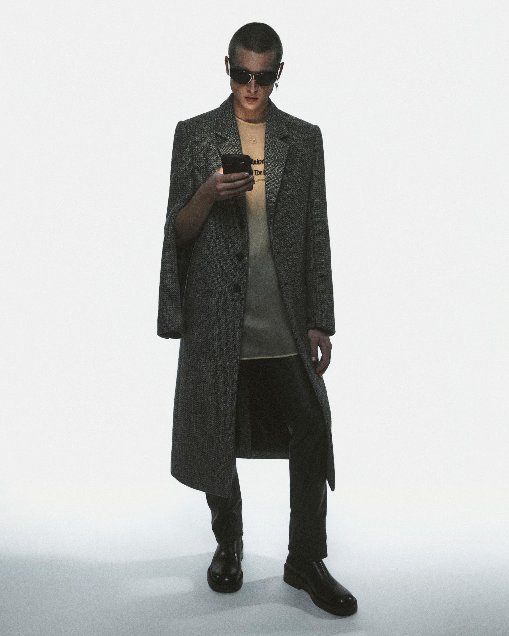 Fashion-forward model wearing a chic gray coat, sunglasses, and stylish black boots for Courrèges.