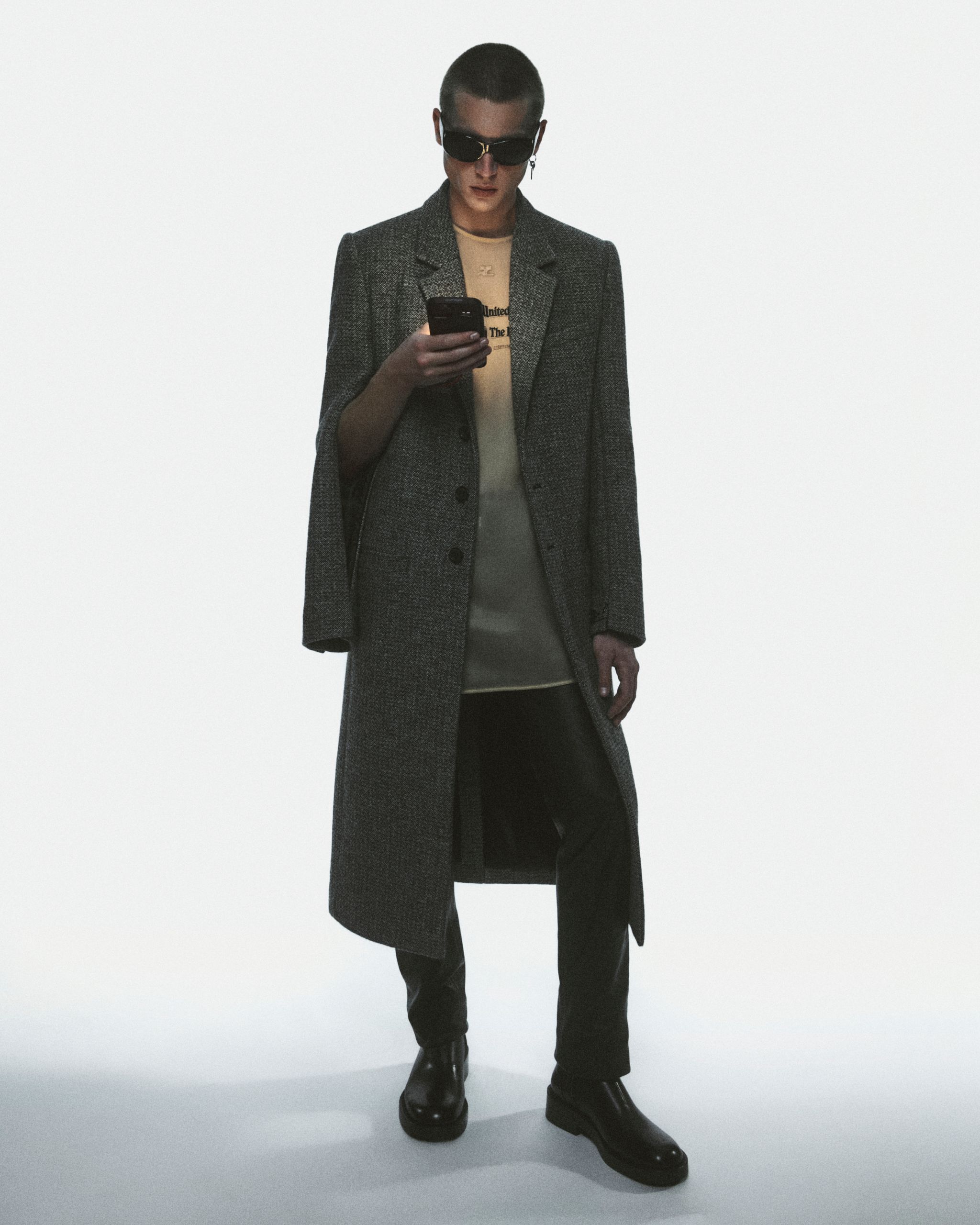 Mannequin portant un long manteau, lunettes de soleil et vêtements élégants pour Courrèges en ligne.