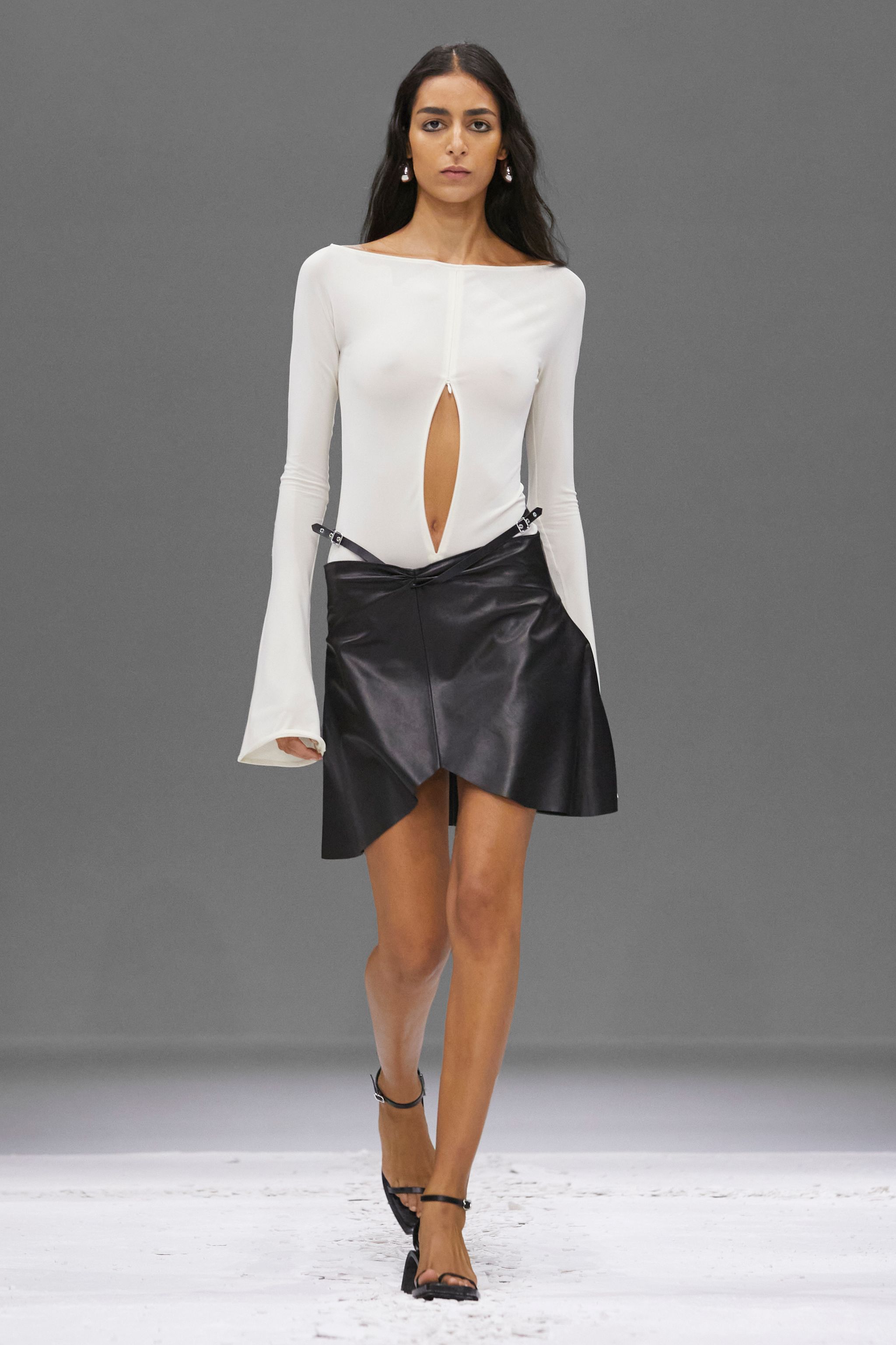 Elegant white top with a keyhole cutout, paired with a black leather asymmetric skirt, Courrèges fashion.
