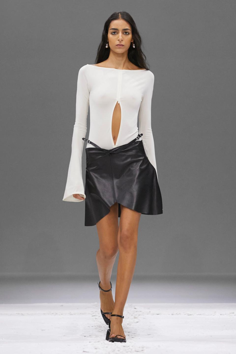 Elegant white top with a keyhole cutout, paired with a black leather asymmetric skirt, Courrèges fashion.