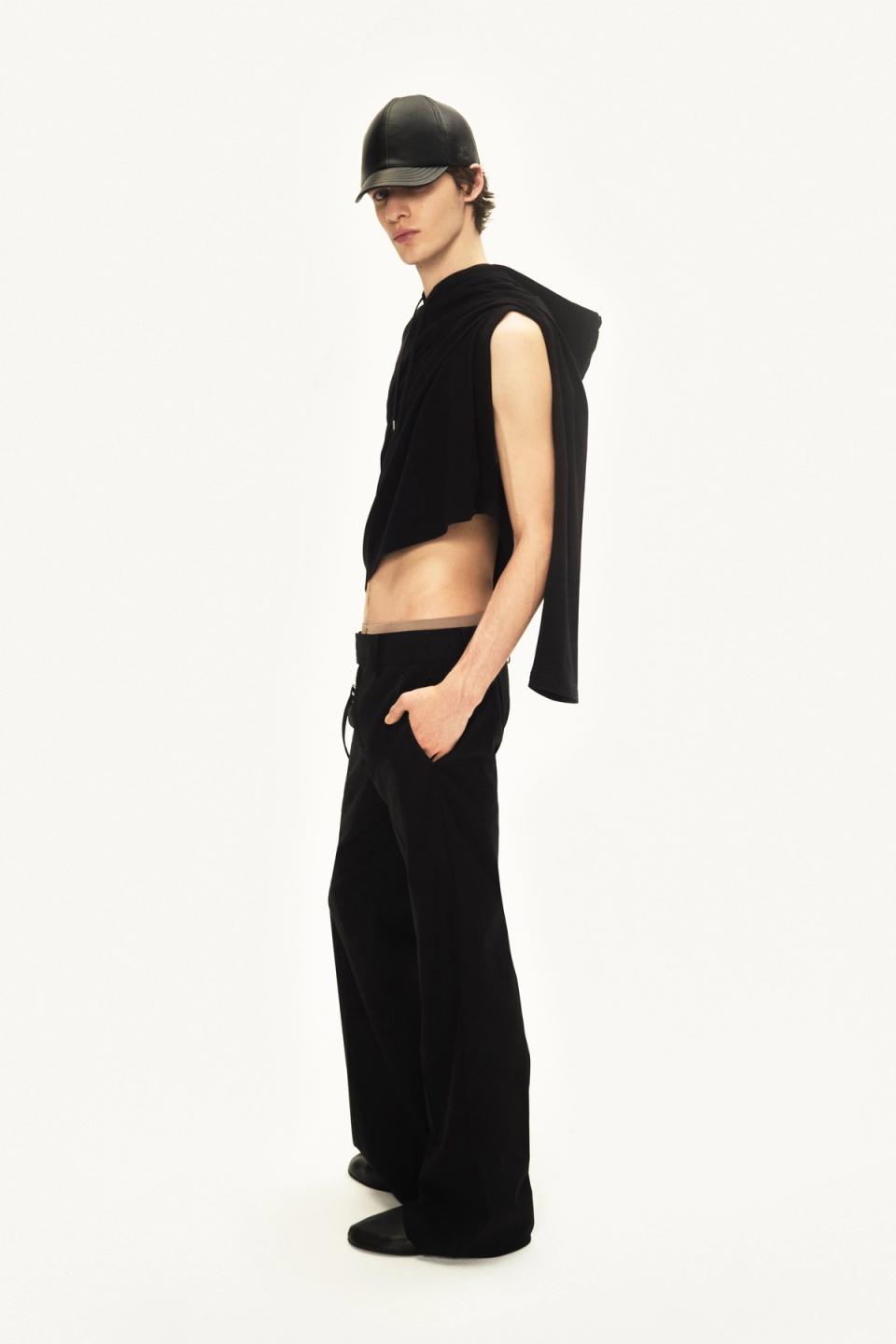 Fashion model in black sleeveless hoodie, black pants, and leather cap for Courrèges fashion brand.