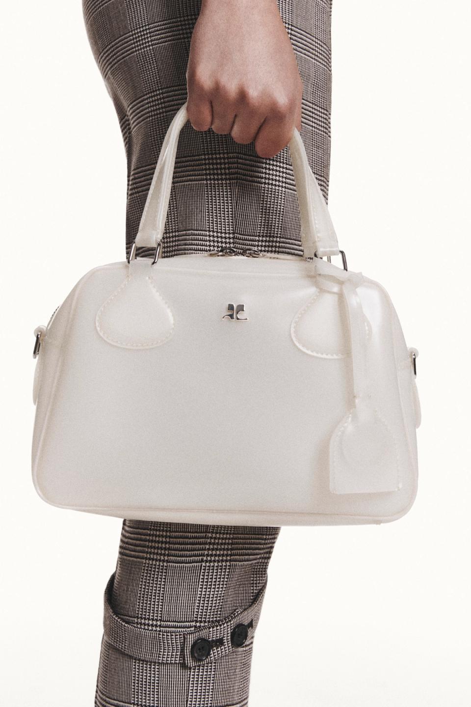 Elegant white handbag by Courrèges held in a stylish person's hand for fashion ecommerce.