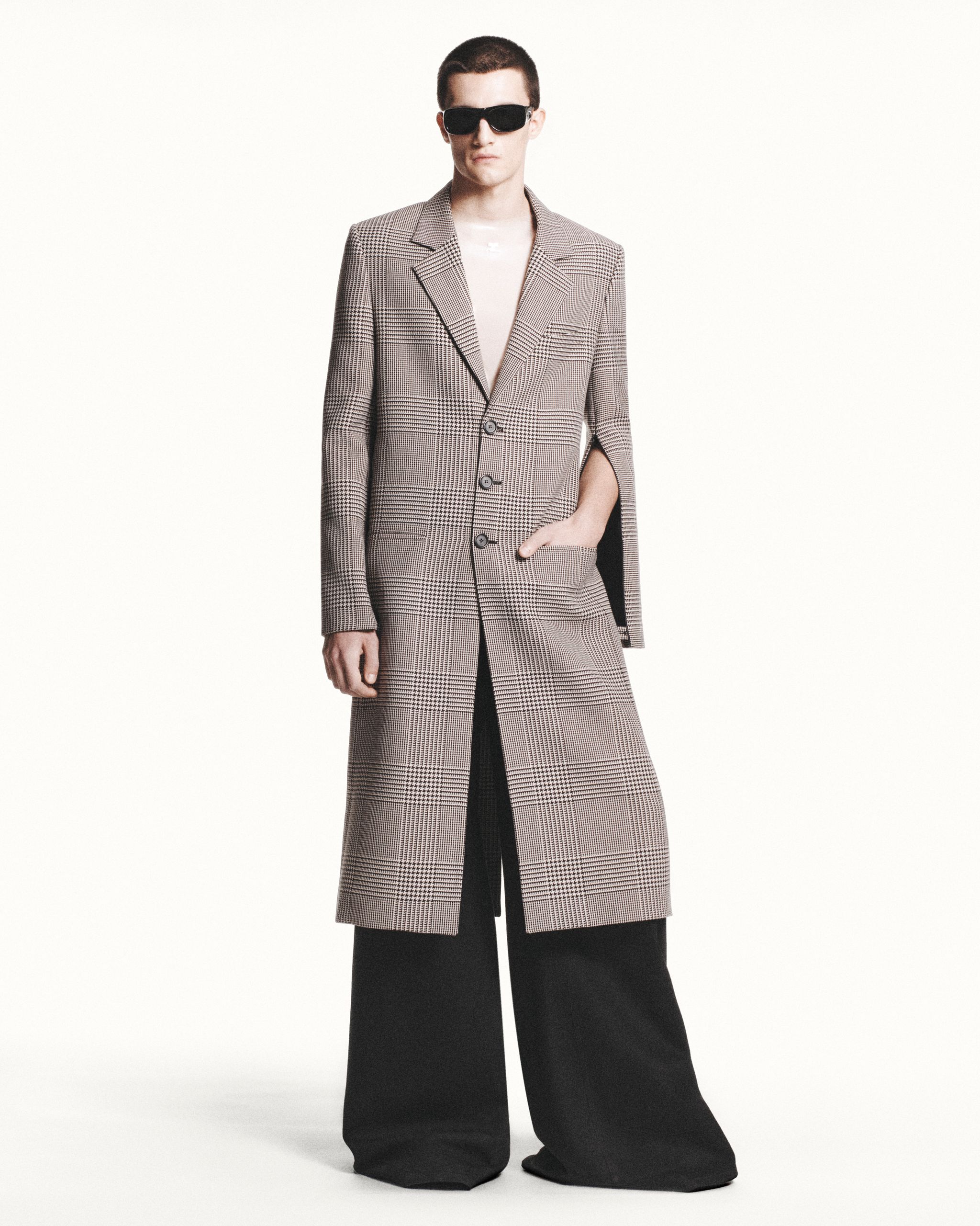 Elegant fashion model in a tailored plaid coat, black wide-leg pants, and sunglasses for Courrèges.