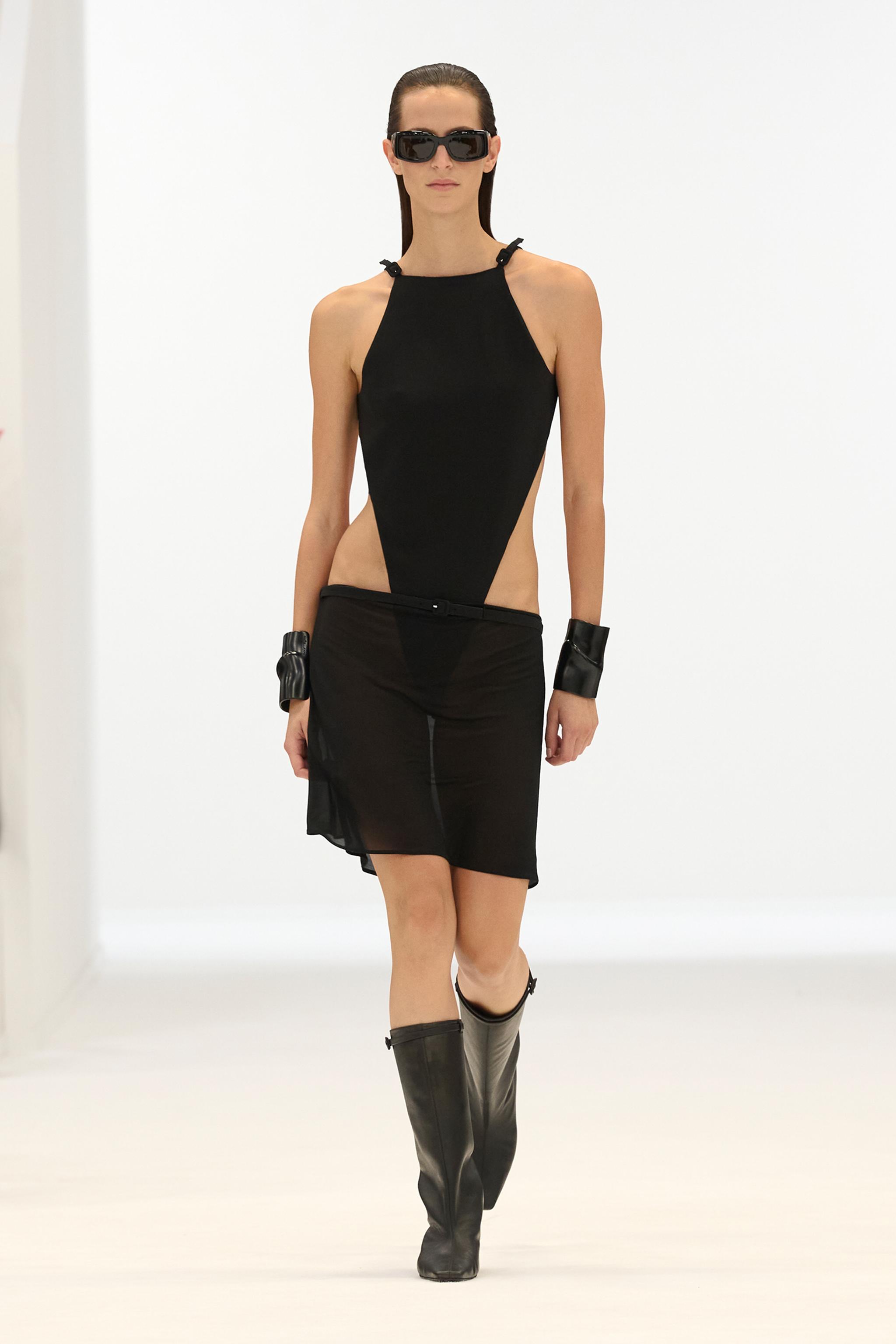 Elegant black designer dress with cut-out sides, sunglasses, and stylish accessories by Courrèges.