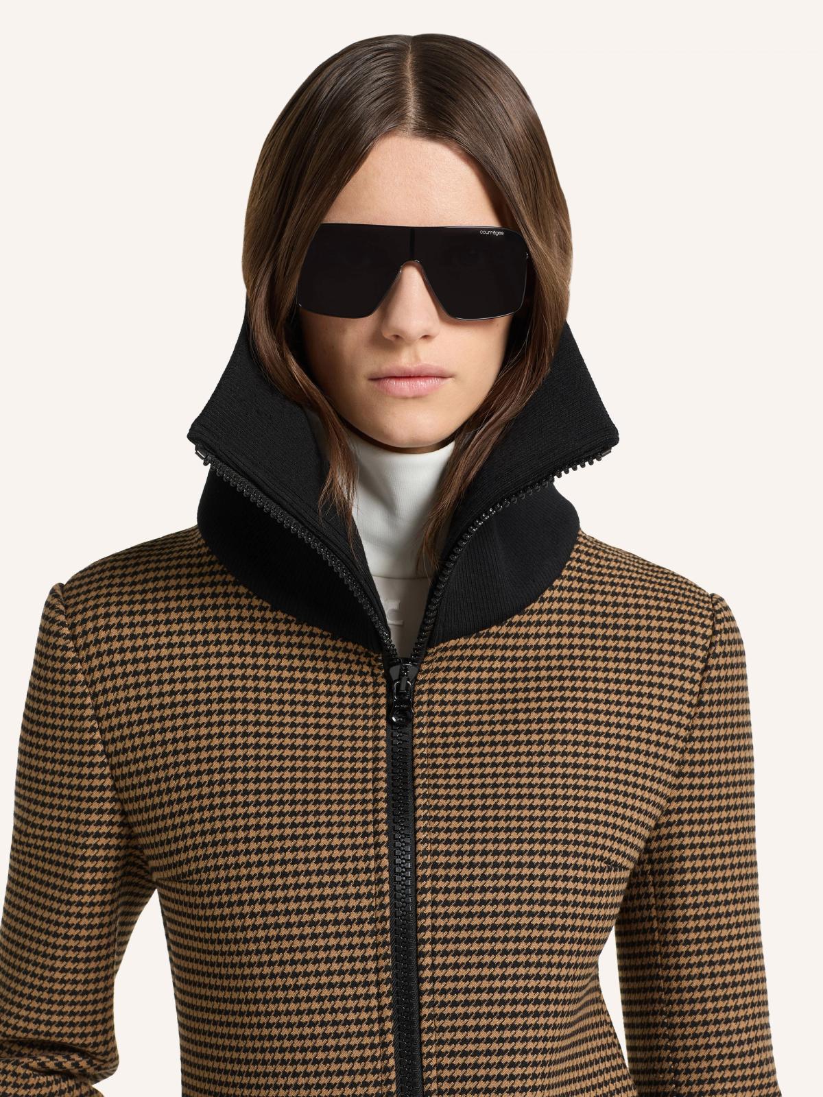 Fashion-forward woman wearing black oversized sunglasses and a stylish zip-up jacket from Courrèges.