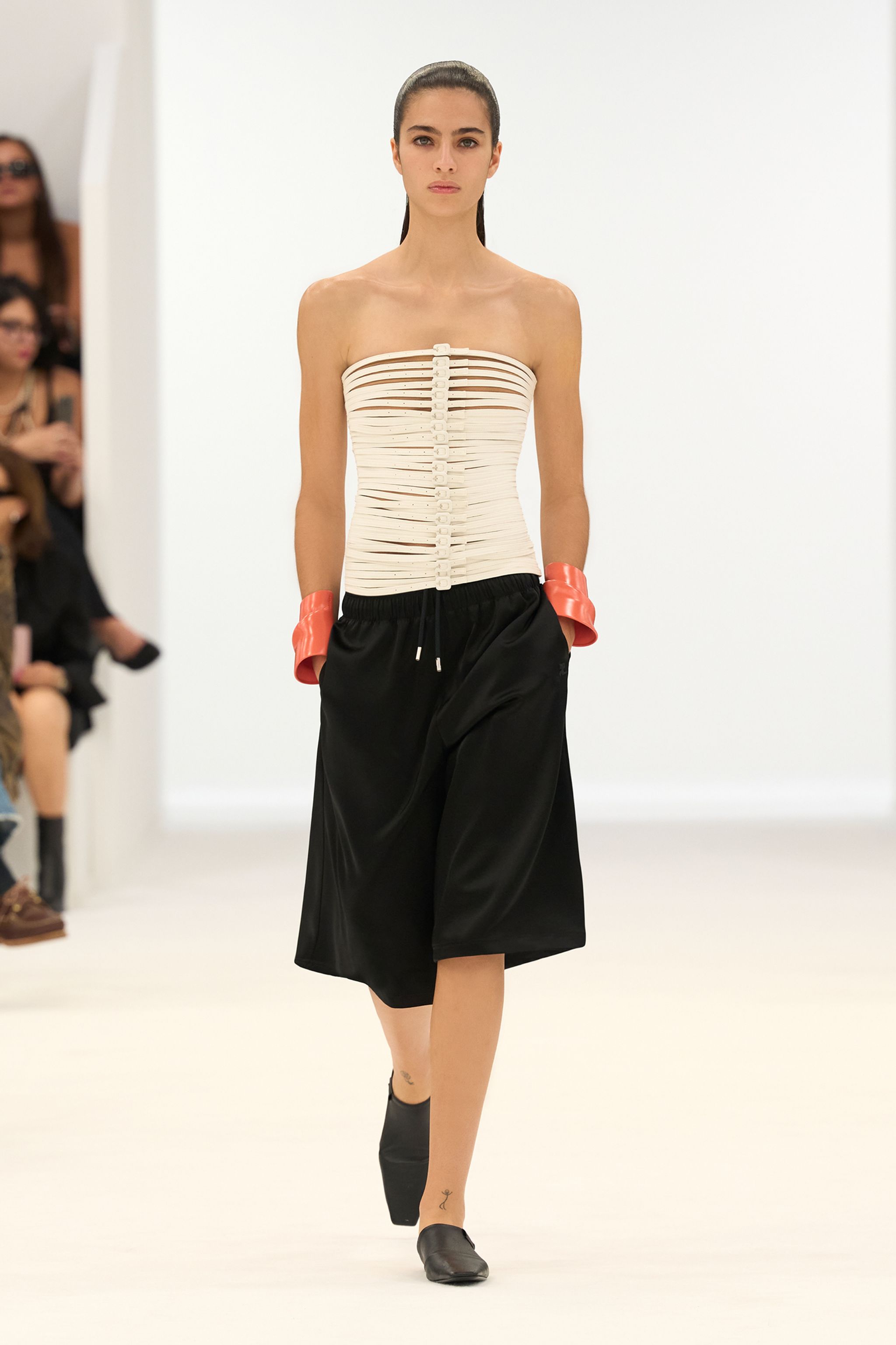Elegant model in a minimalist Courrèges fashion show, wearing a sculptural white top and black skirt.