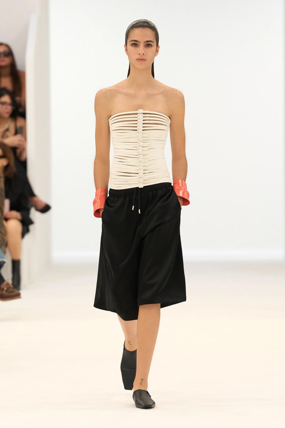 Elegant model in a minimalist Courrèges fashion show, wearing a sculptural white top and black skirt.