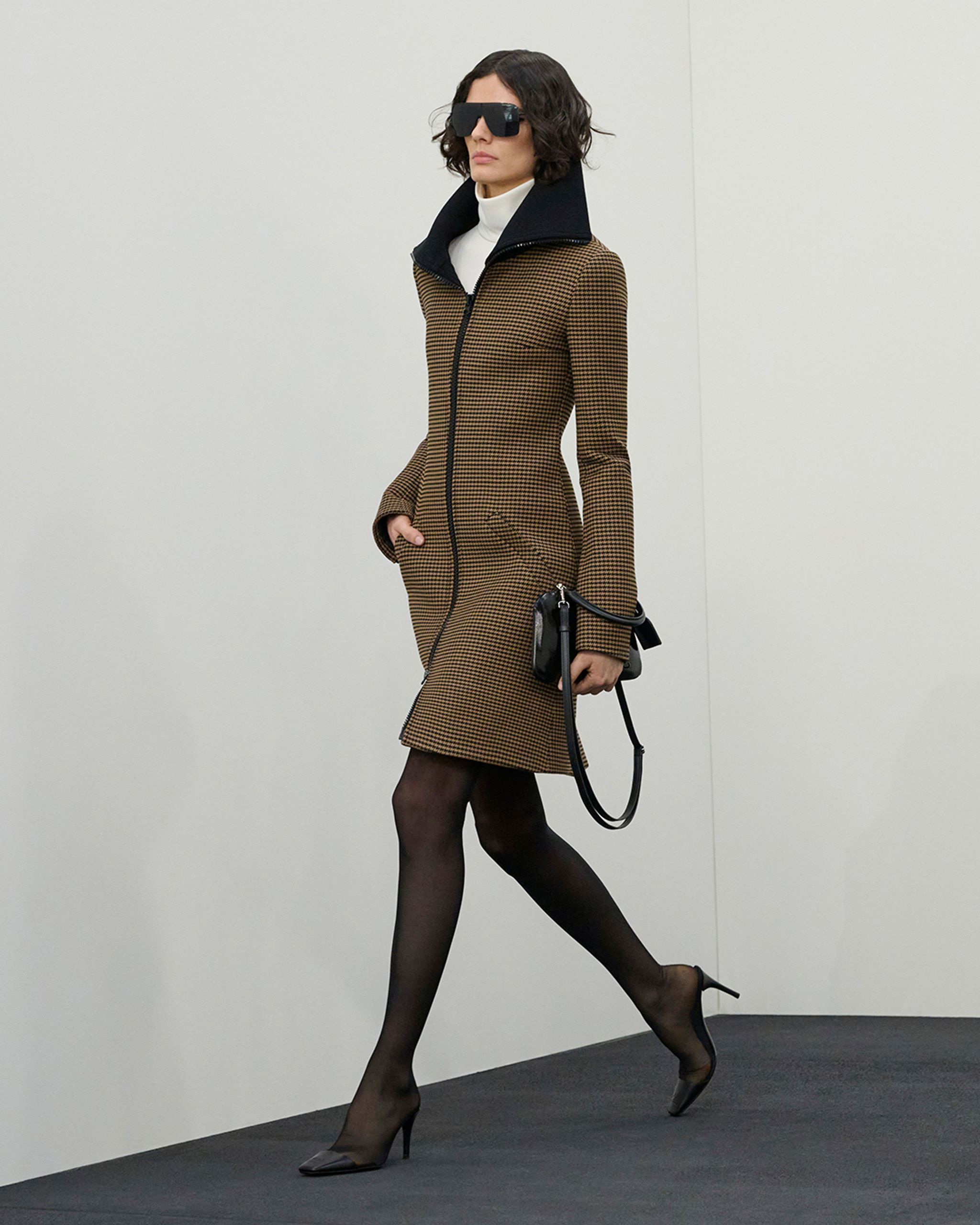 Modèle élégant en manteau pied-de-poule, collants noirs, talons et lunettes de soleil oversized Courrèges.