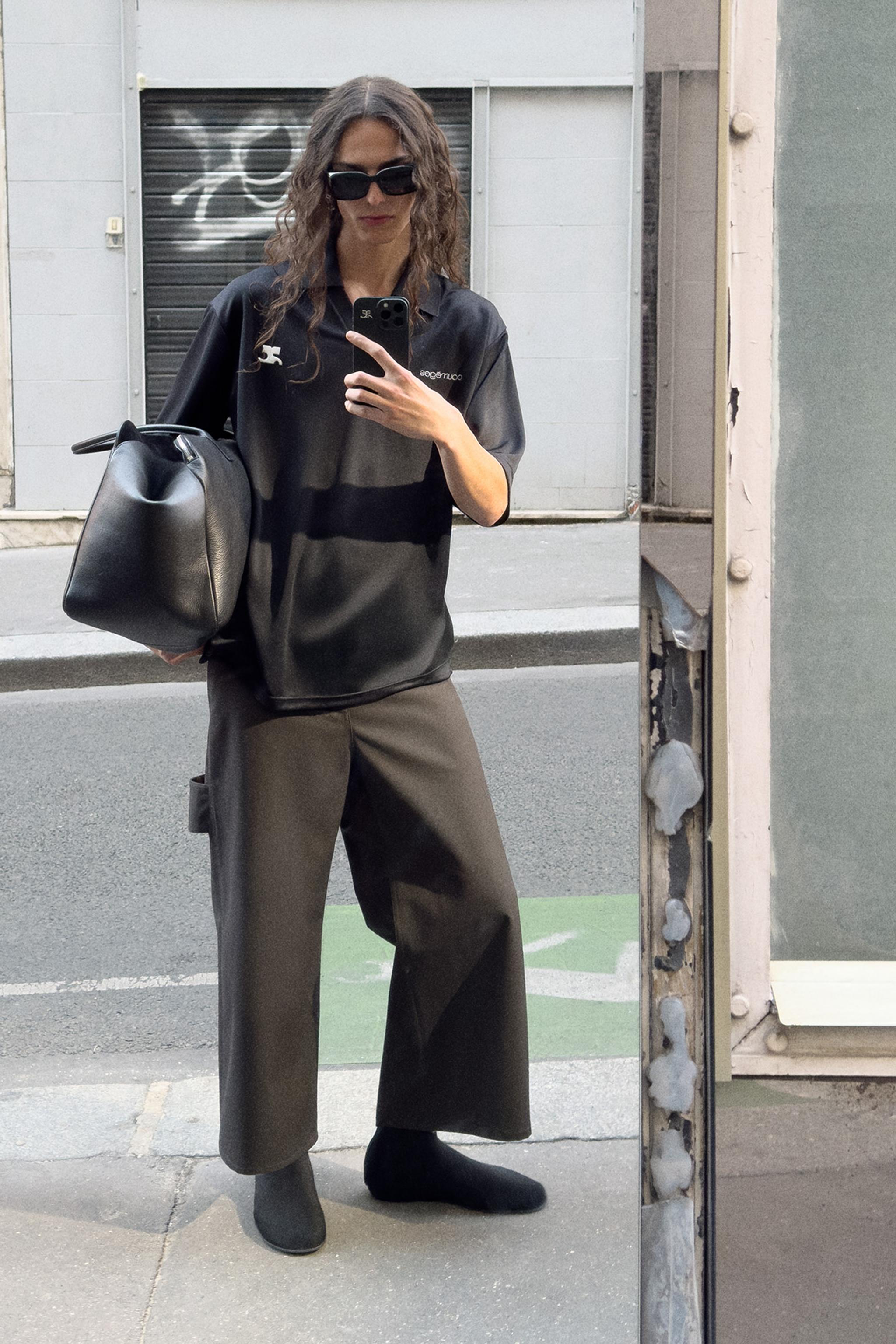 Elegant woman in black Courrèges outfit taking a mirror selfie outdoors for fashion website