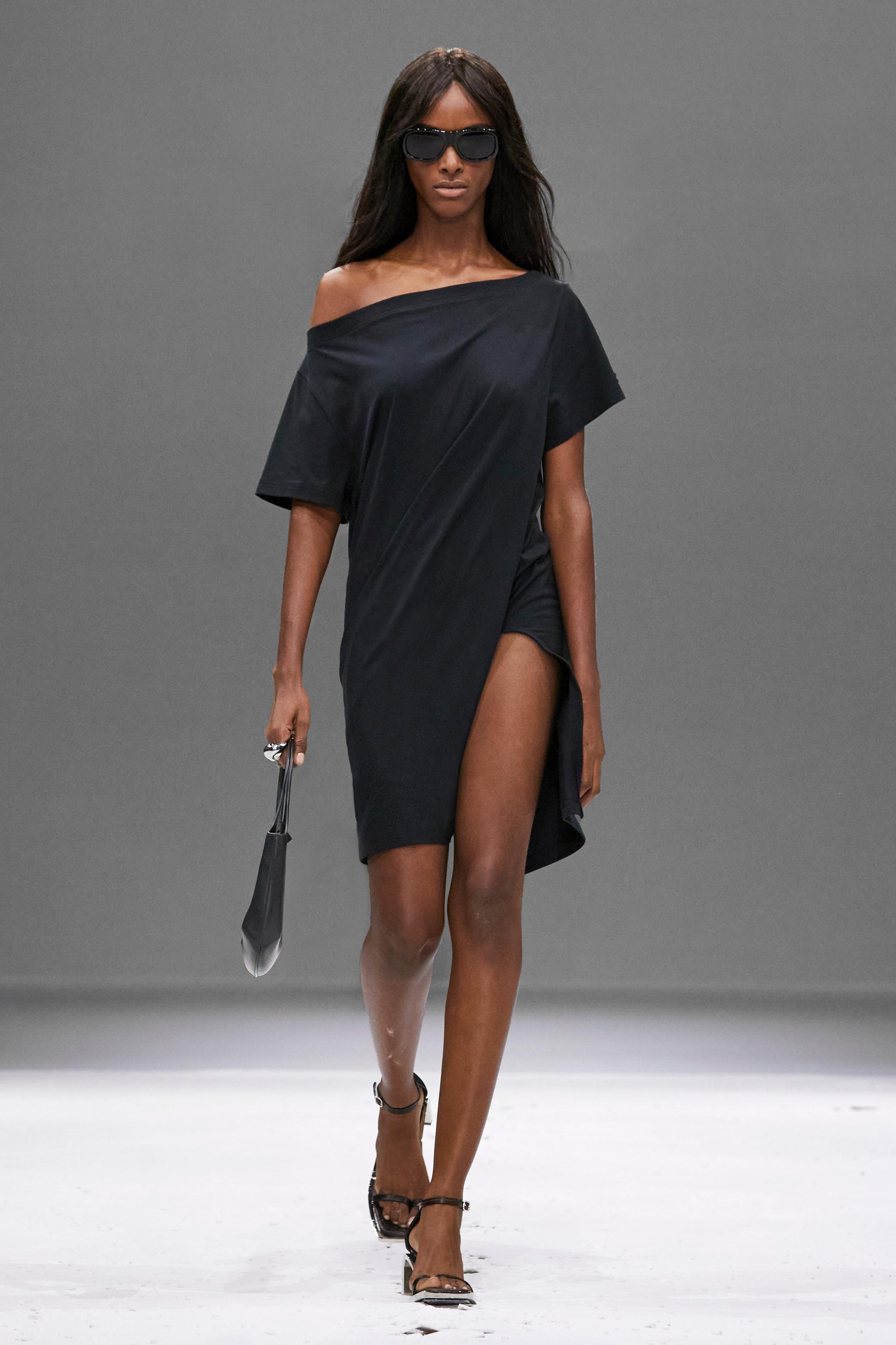 Elegant black off-shoulder dress with a high slit, showcased by Courrèges on a runway.
