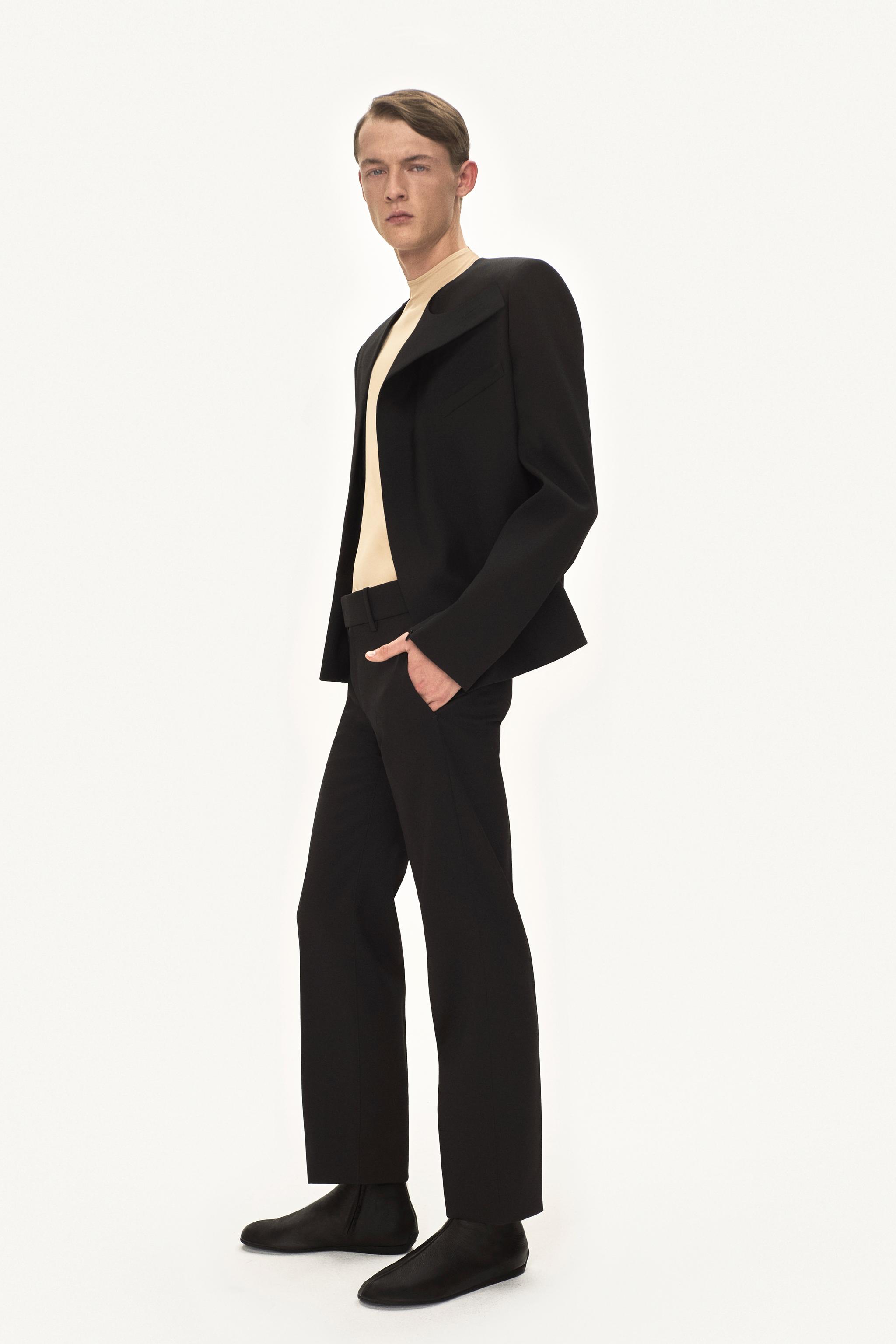 Modèle masculin élégant en blazer et pantalon noirs, mettant en valeur la mode Courrèges.