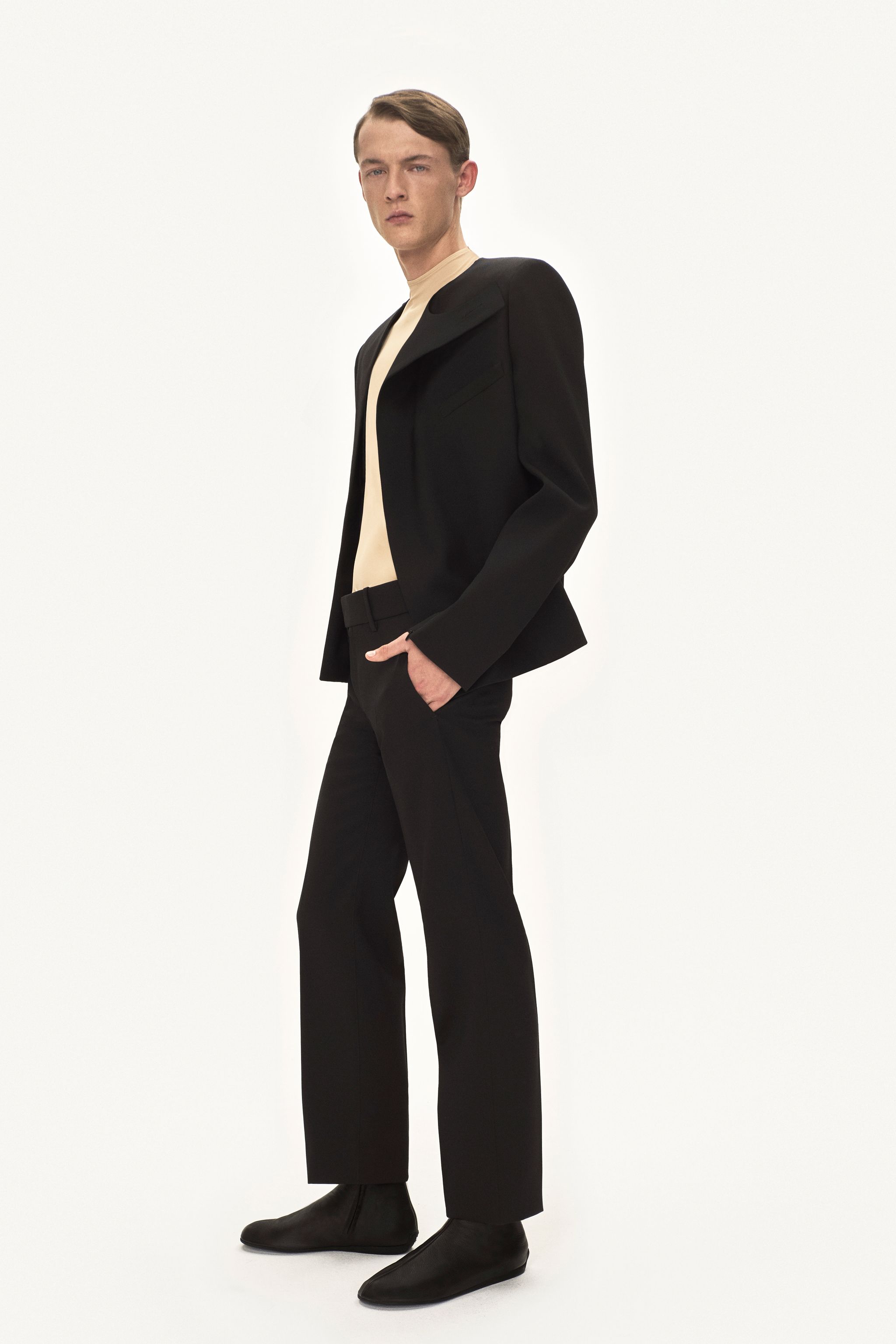 Elegant male model in black suit, beige turtleneck, showcasing Courrèges fashion brand.