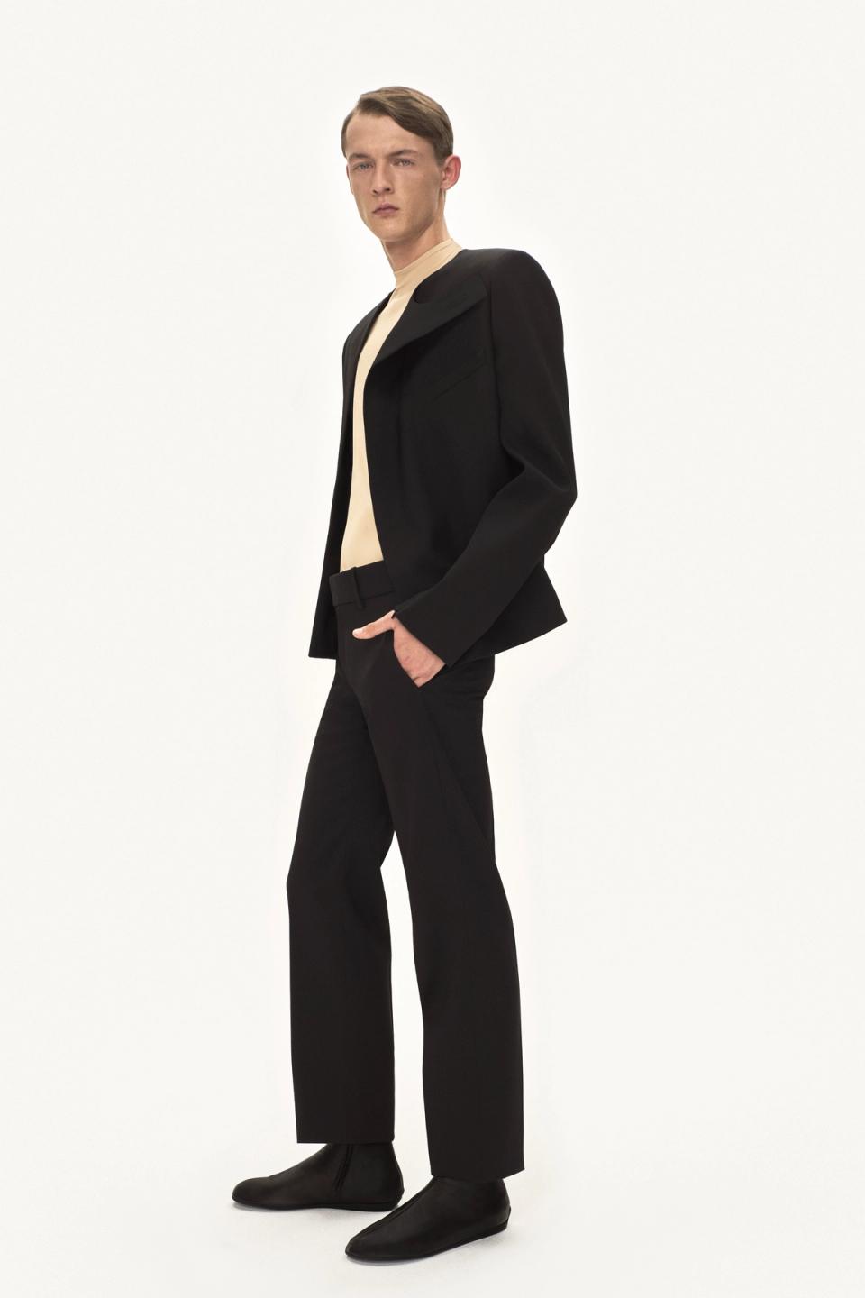 Elegant male model in black suit, beige turtleneck, showcasing Courrèges fashion brand.