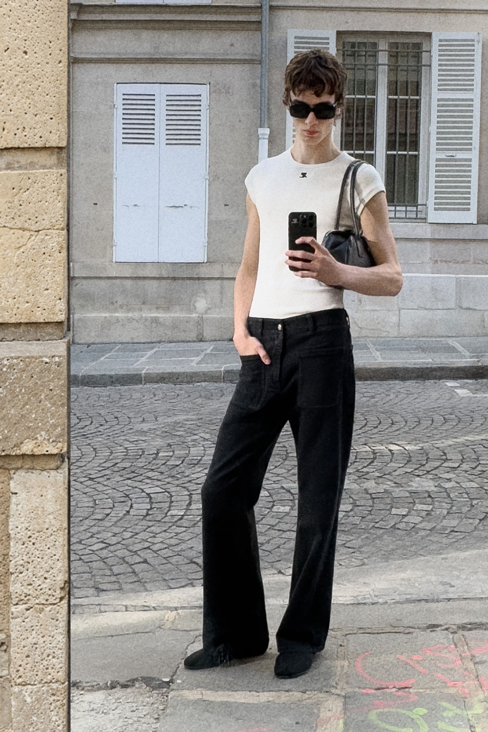 Elegant fashion-forward woman with short hair, sunglasses, white top, black pants and a handbag.