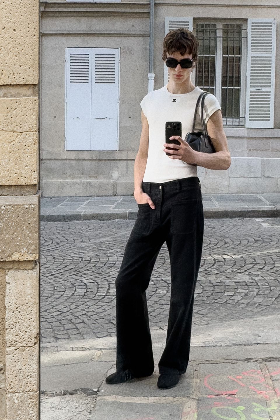 Elegant fashion-forward woman with short hair, sunglasses, white top, black pants and a handbag.