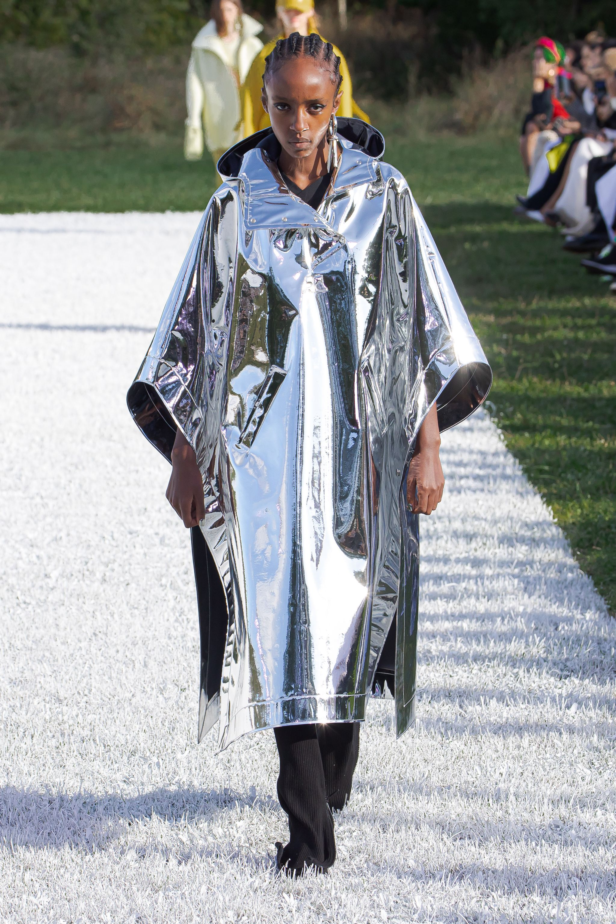 Elegant model wearing a shiny, metallic cloak on the Courrèges runway for an ecommerce site.