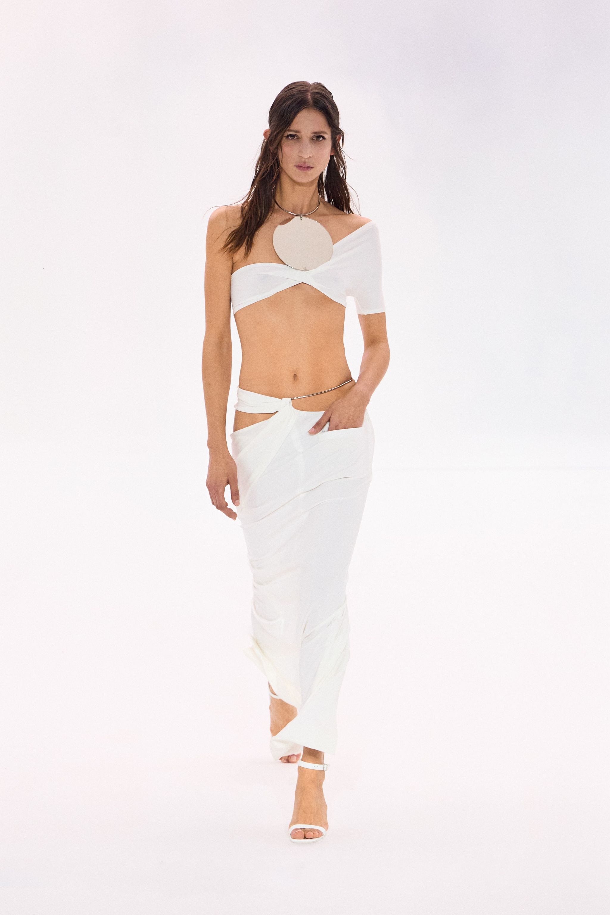 Elegant white crop top and skirt by Courrèges, modeled on a runway against a plain background.