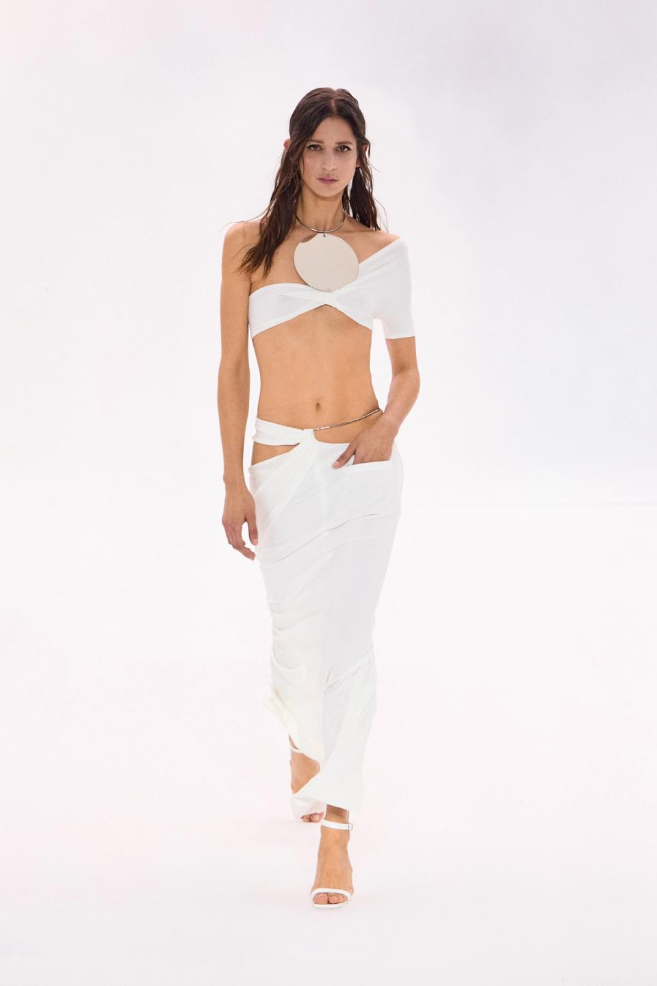 Elegant white crop top and skirt by Courrèges, modeled on a runway against a plain background.