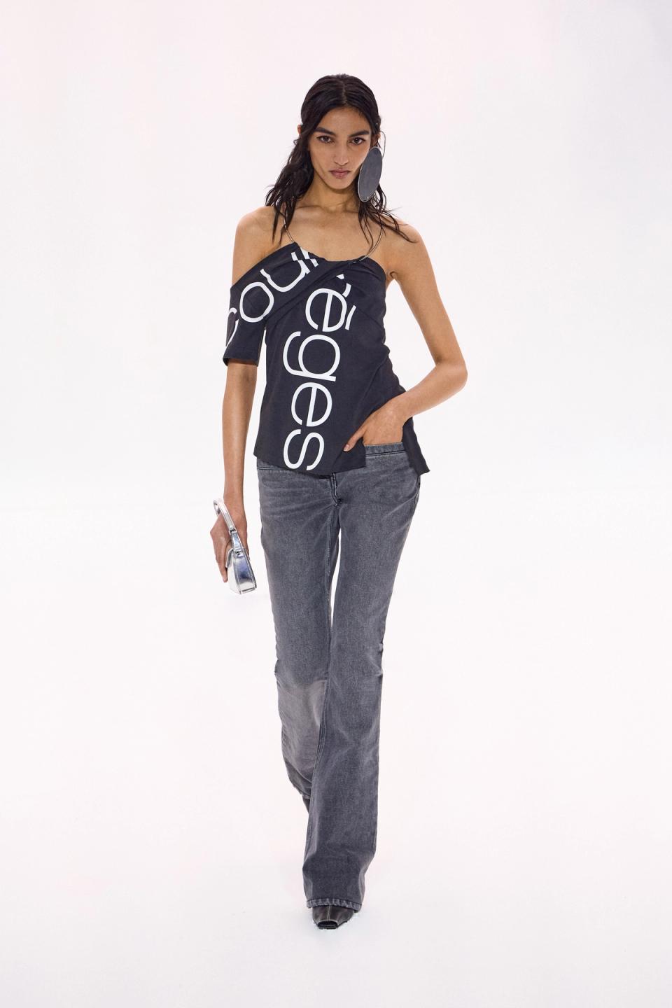 Elegant model in casual Courrèges fashion wearing a black logo top and gray jeans.