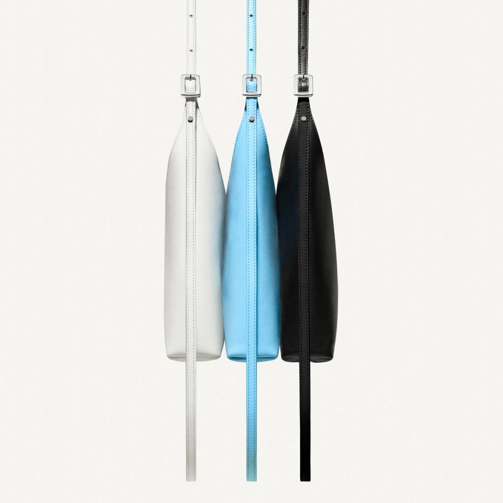 Elegant vertical view of three Courrèges minimalist leather handbags in white, blue, and black.