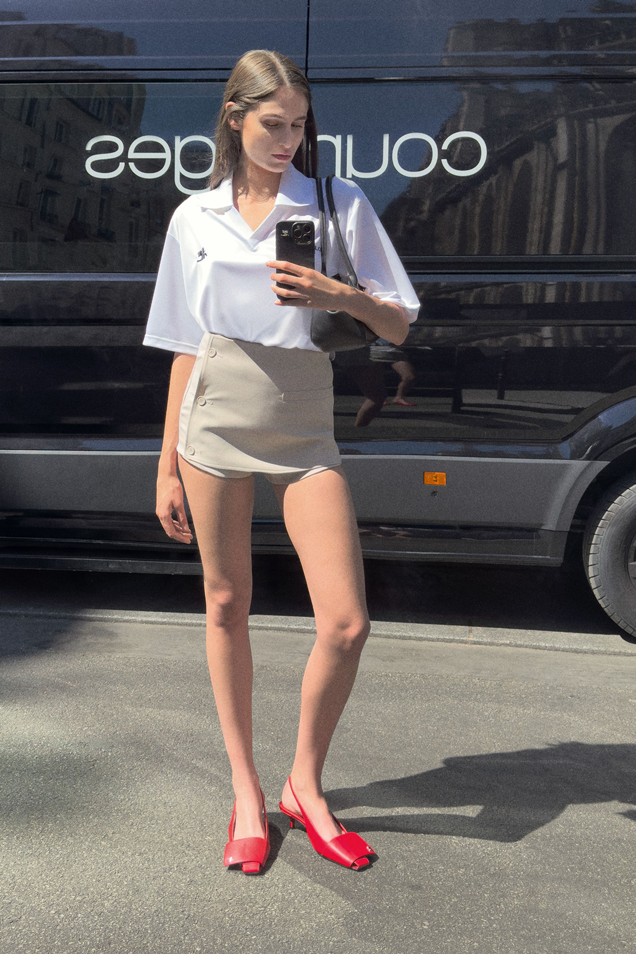 Fashionable woman taking a mirror selfie outdoors, wearing Courrèges minimalist chic attire.