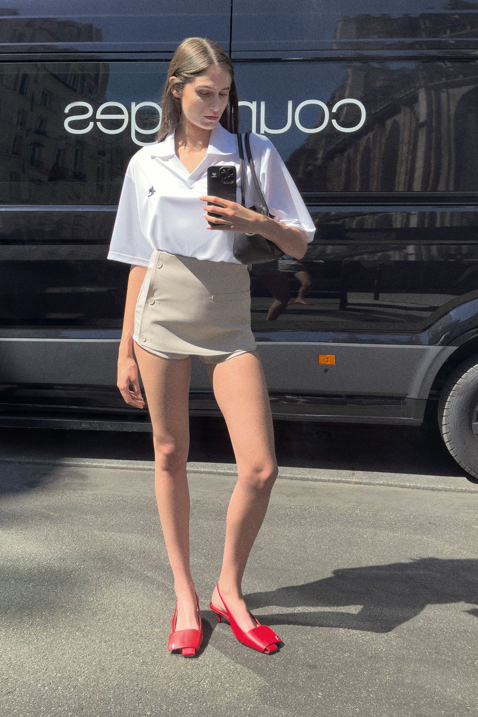 Fashionable woman taking a mirror selfie outdoors, wearing Courrèges minimalist chic attire.