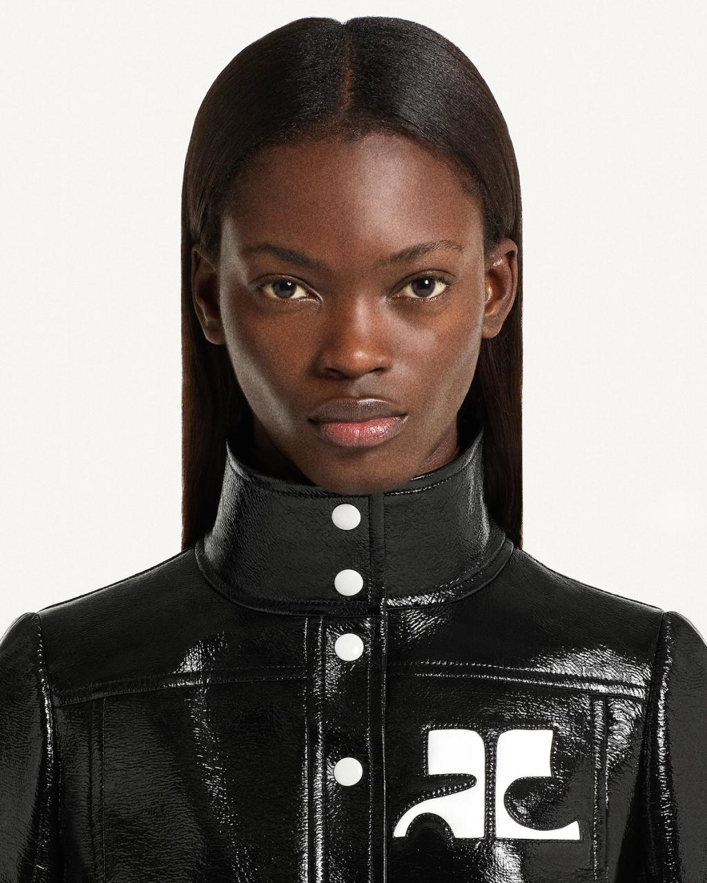 Elegant model wearing a black Courrèges patent leather jacket, showcasing modern fashion.