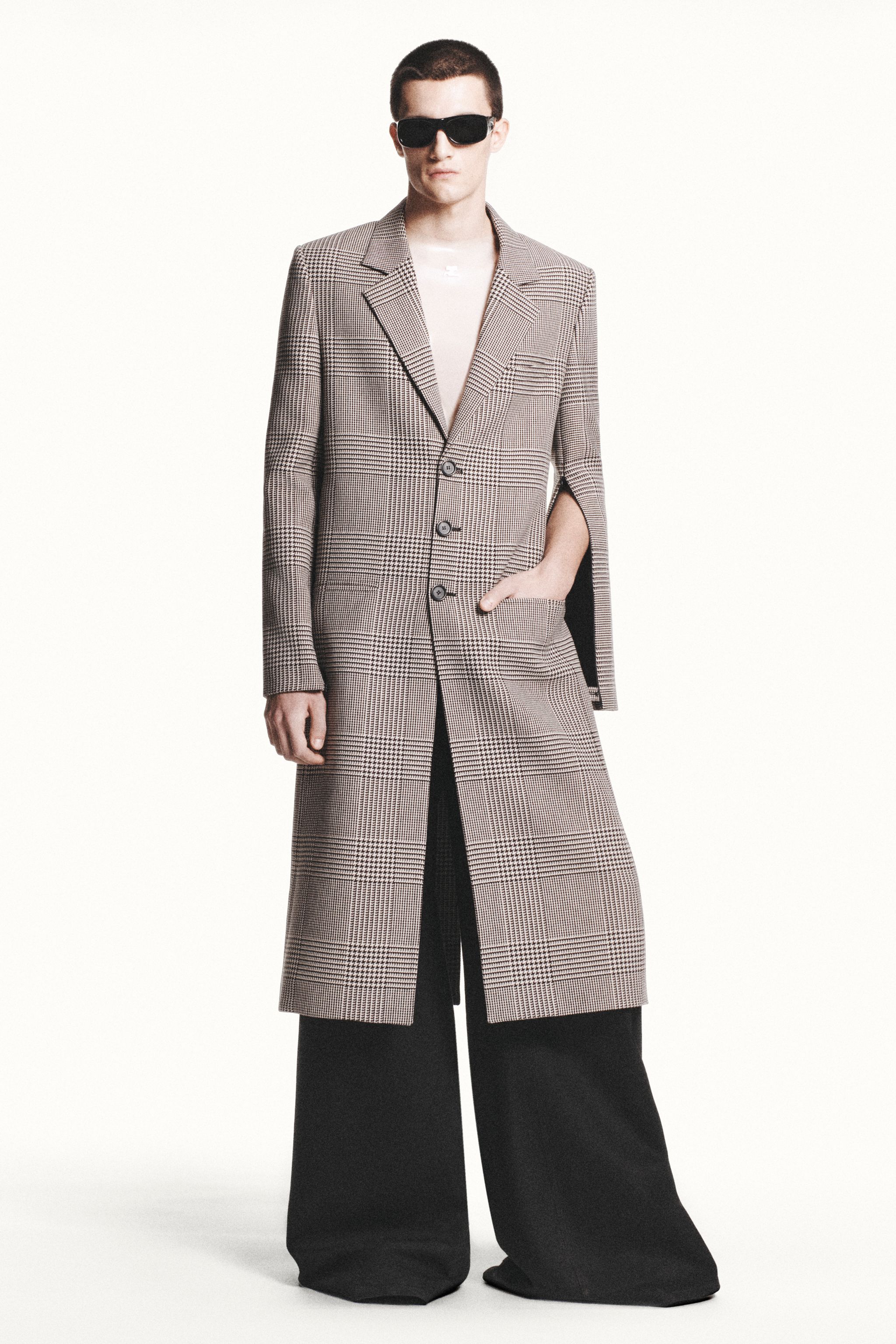 Elegant model in checked coat and wide trousers showcasing Courrèges fashion for online shopping.