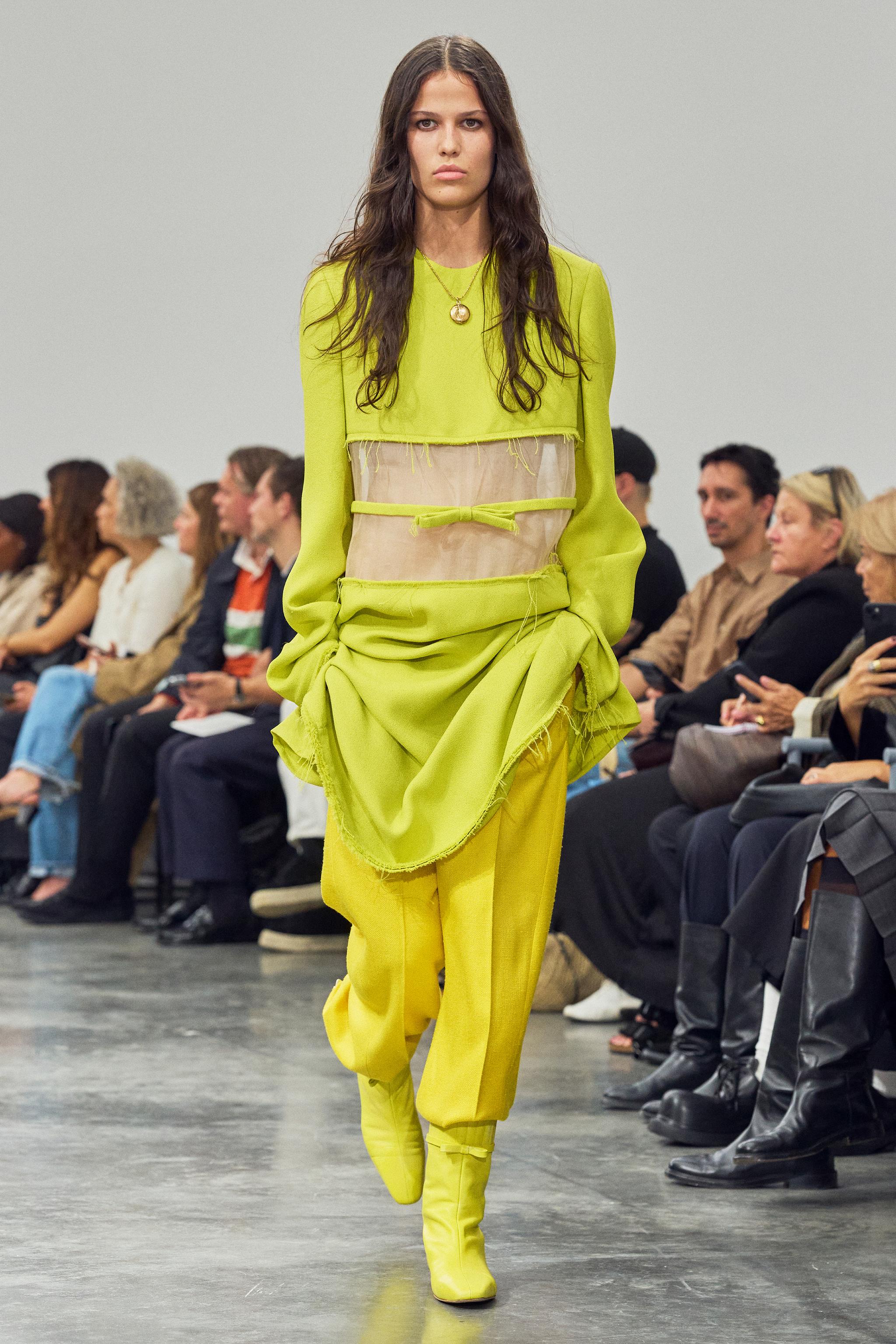 Fashion runway model wearing a vibrant yellow ensemble with sheer details, Courrèges style.