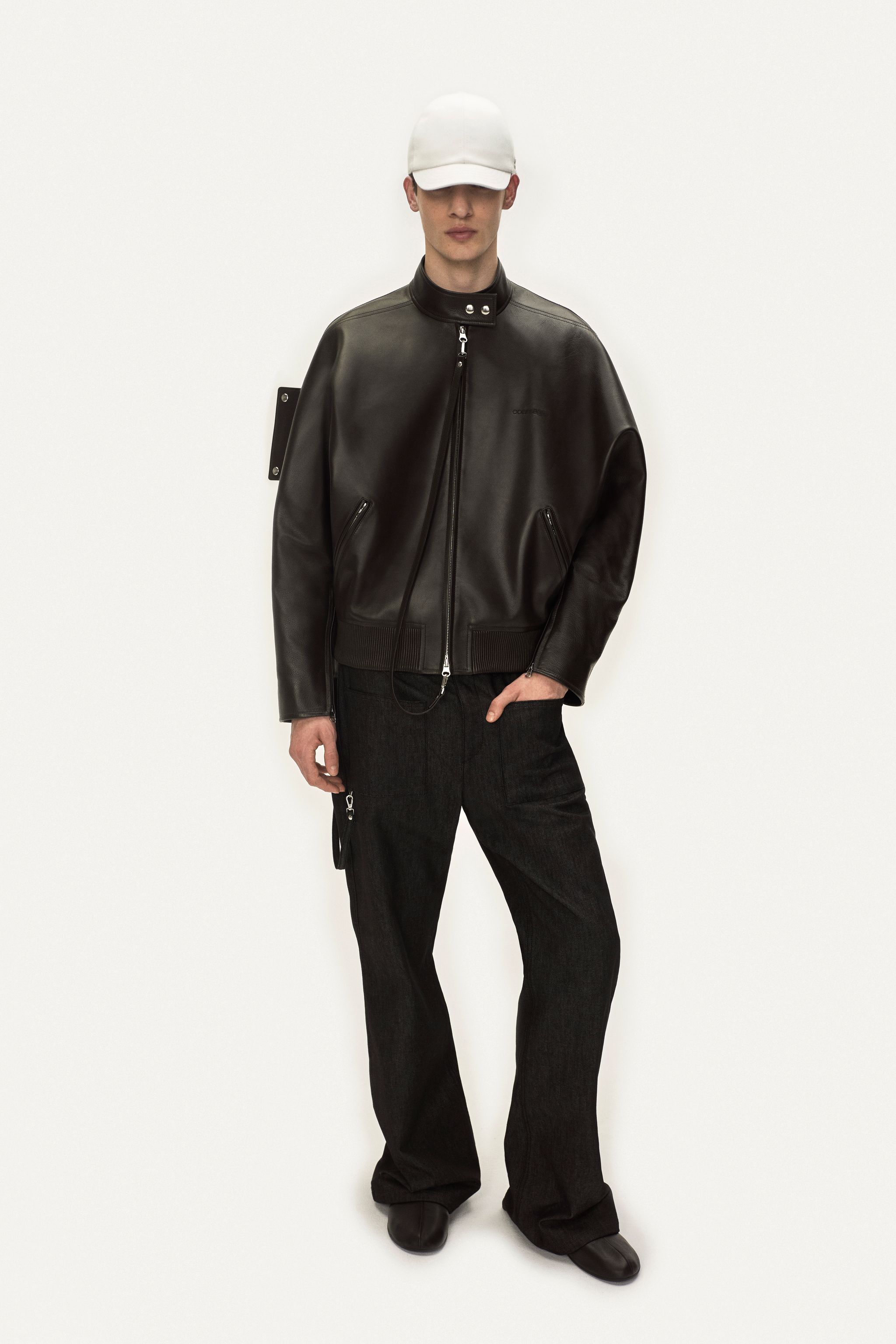 Elegant male model wearing Courrèges black leather jacket and stylish pants for fashion appeal.