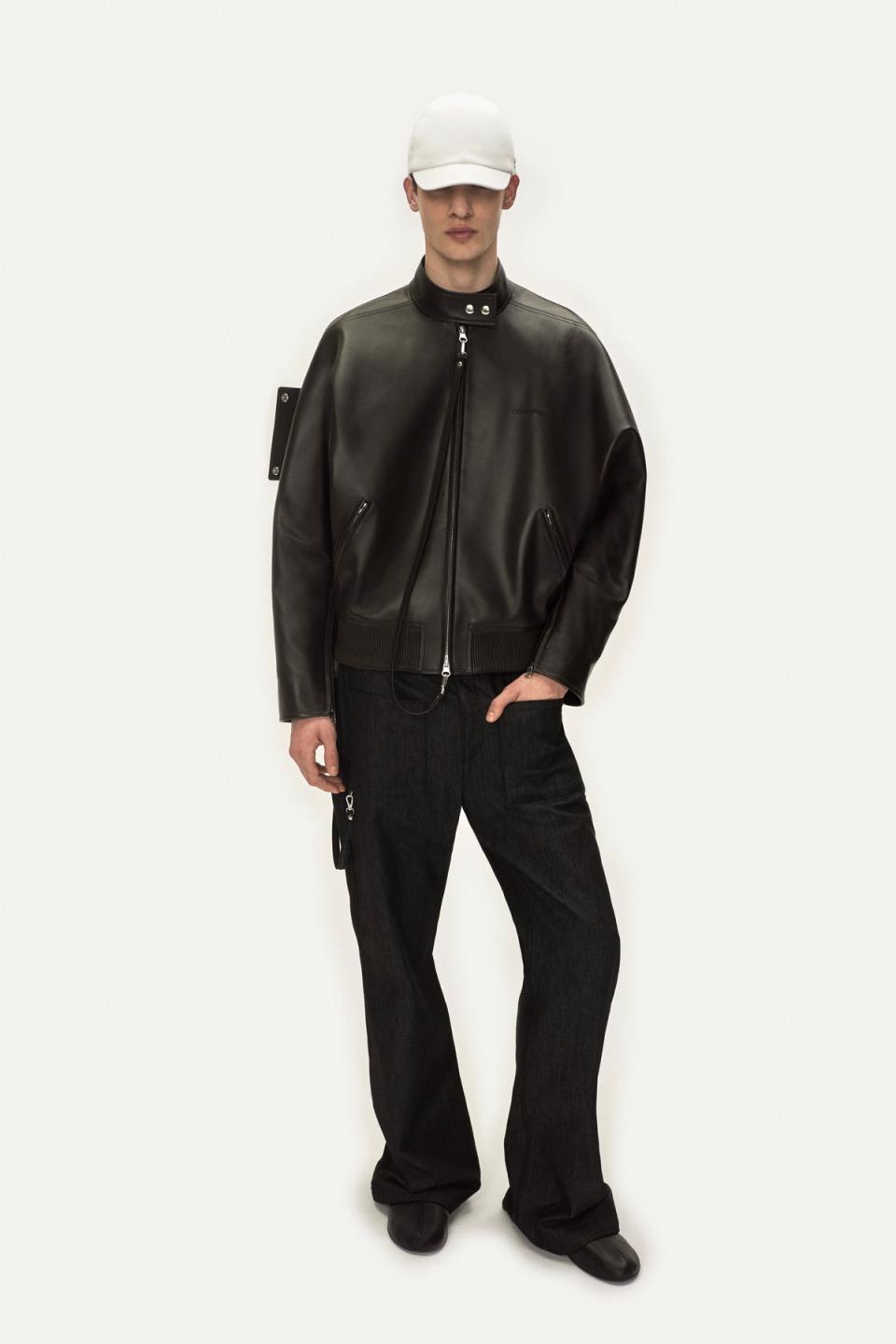 Elegant male model wearing Courrèges black leather jacket and stylish pants for fashion appeal.