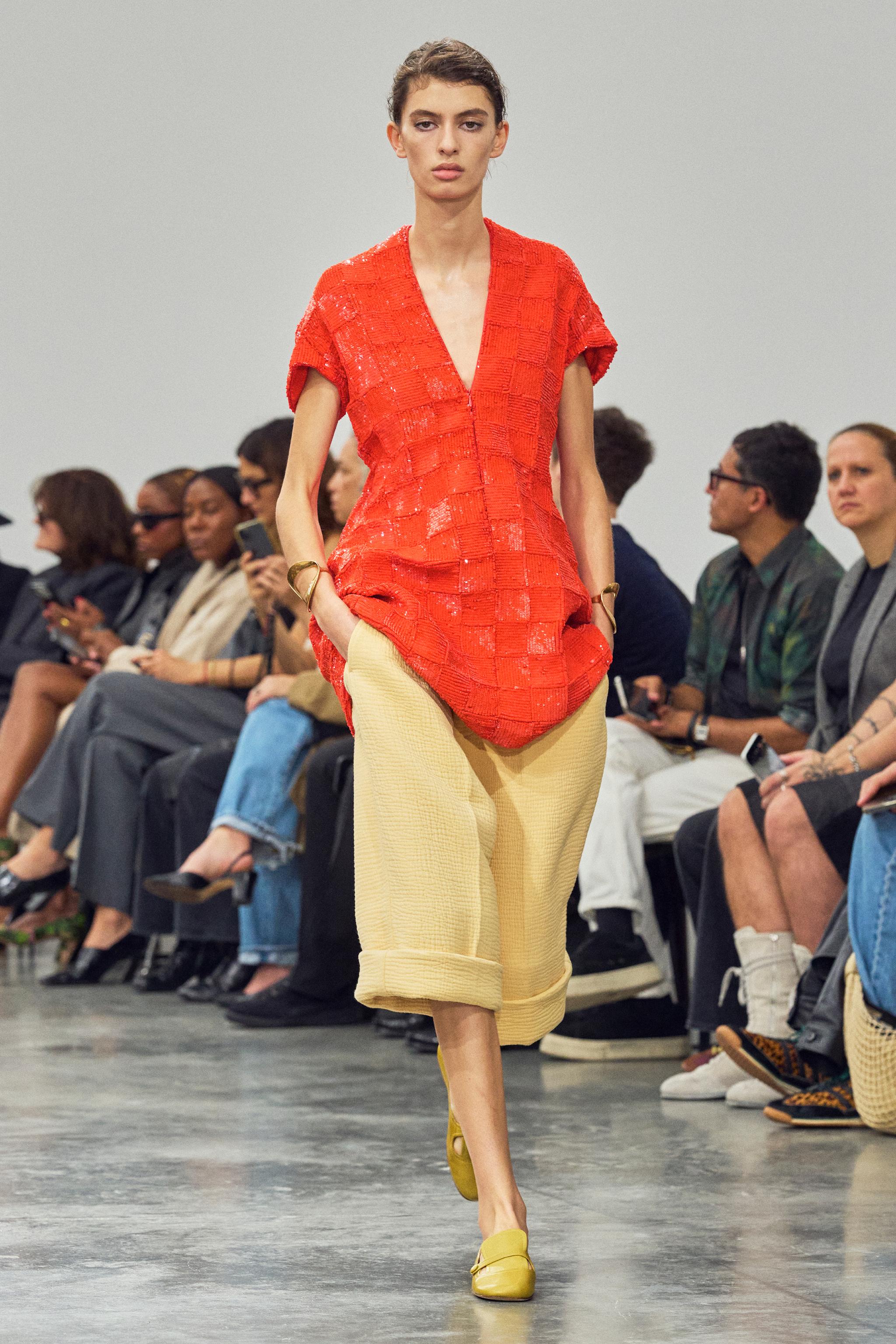 Elegant red textured top with a V-neck, paired with beige wide-leg pants, showcased on a runway.
