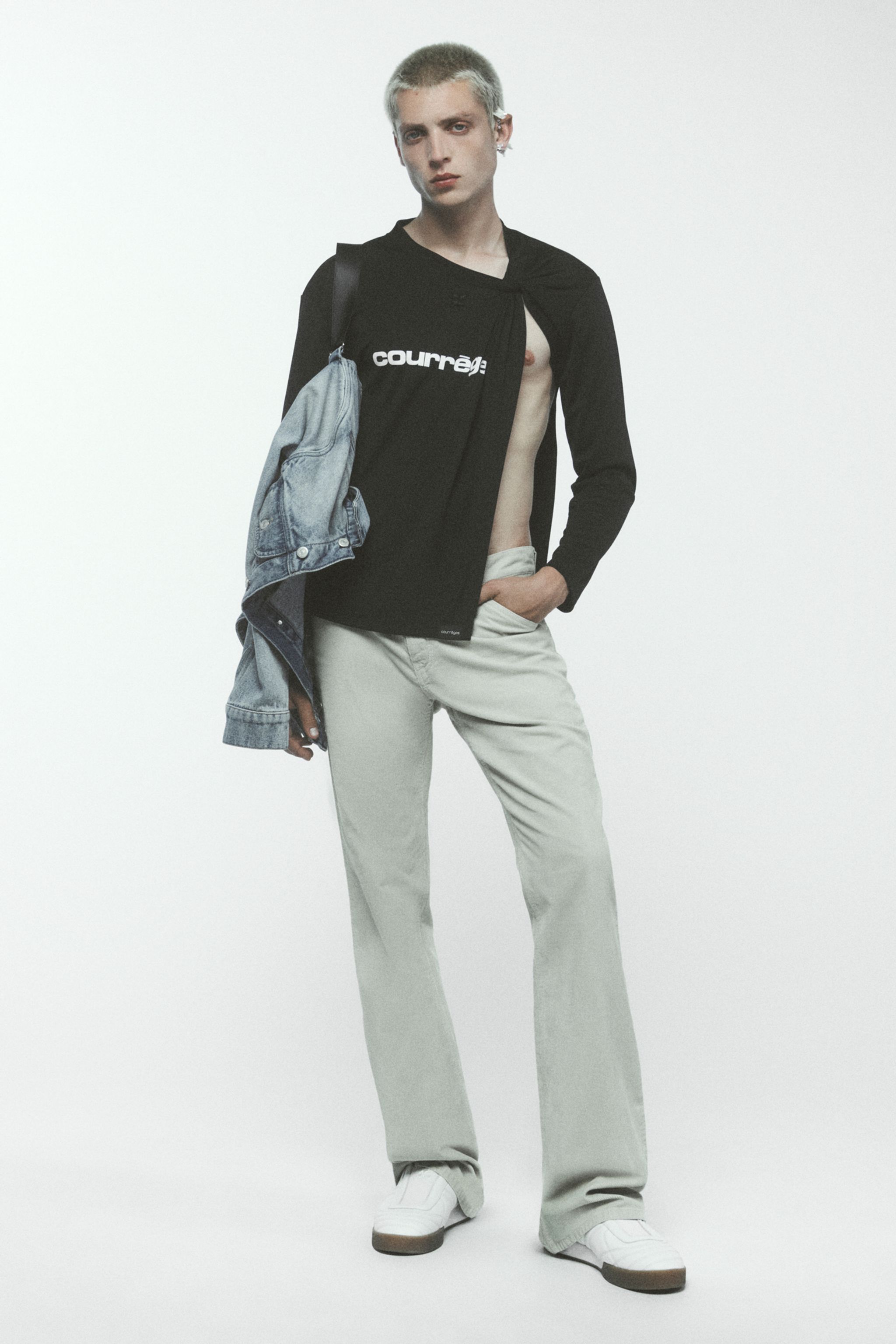Elegant male model in casual Courrèges fashion, featuring a black shirt, beige pants, and denim jacket.