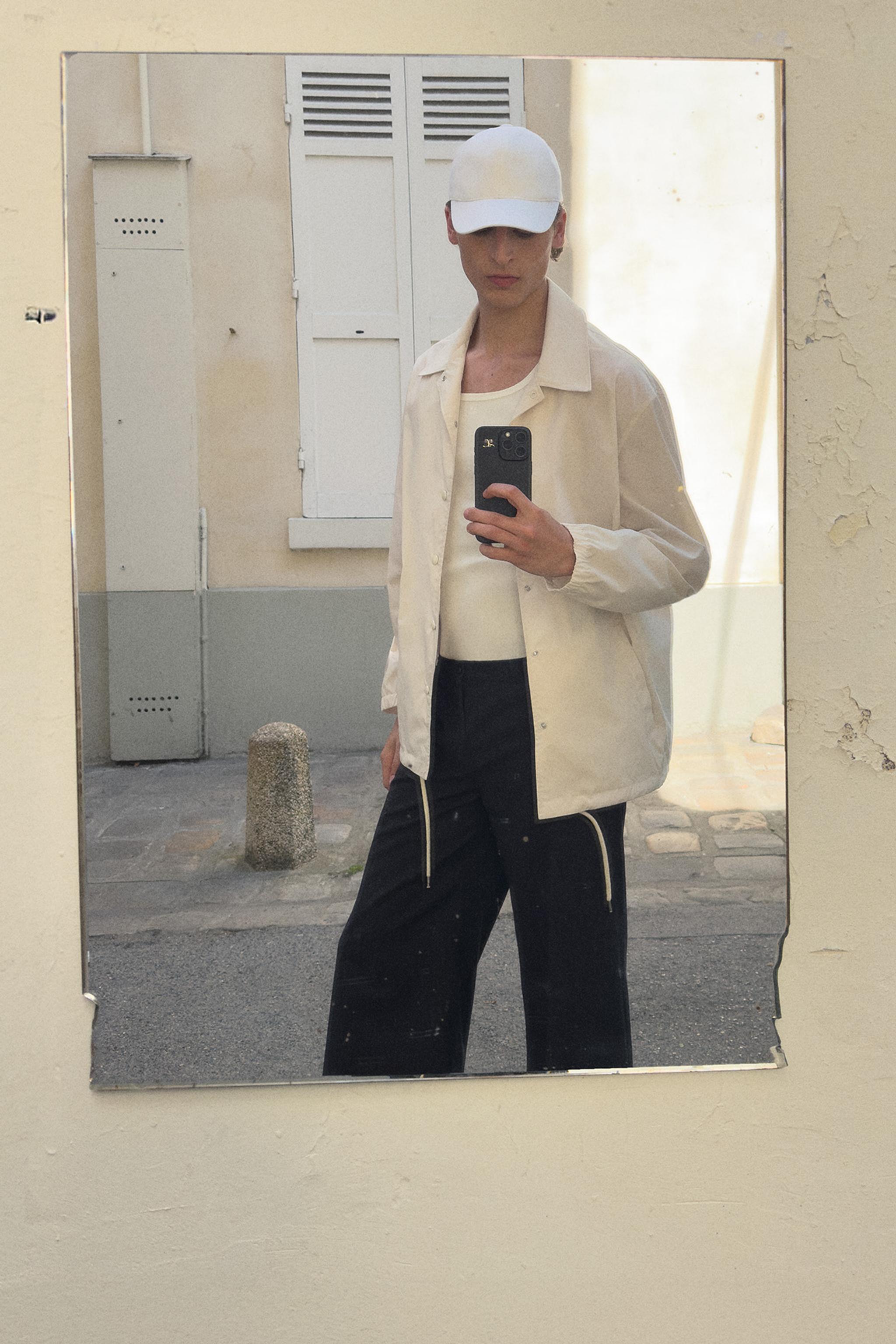 Elegant mirror reflection of a person in a beige and black Courrèges outfit, stylish and minimalist.