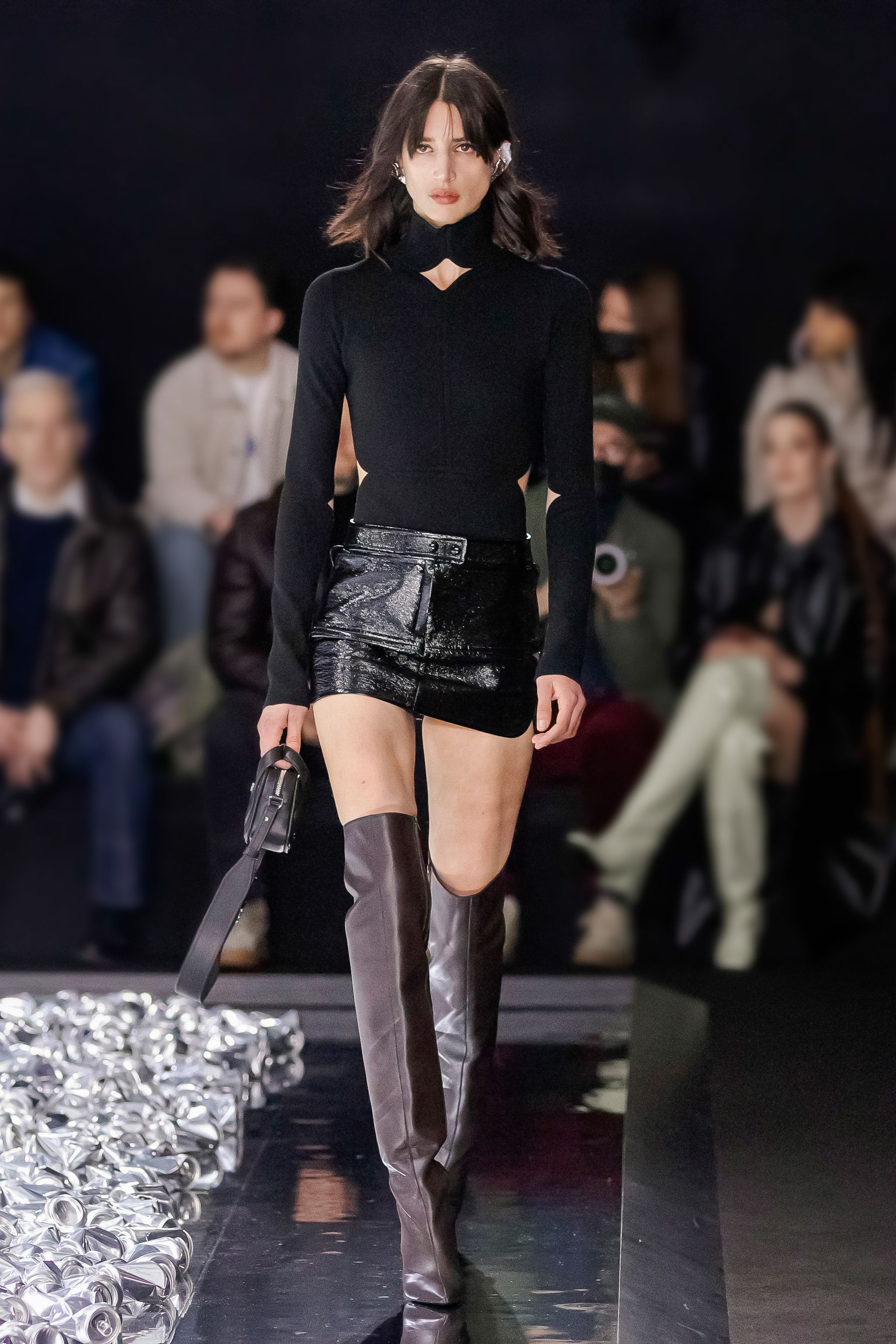 Elegant model at Courrèges fashion show wearing a stylish black top, mini skirt, and thigh-high boots.