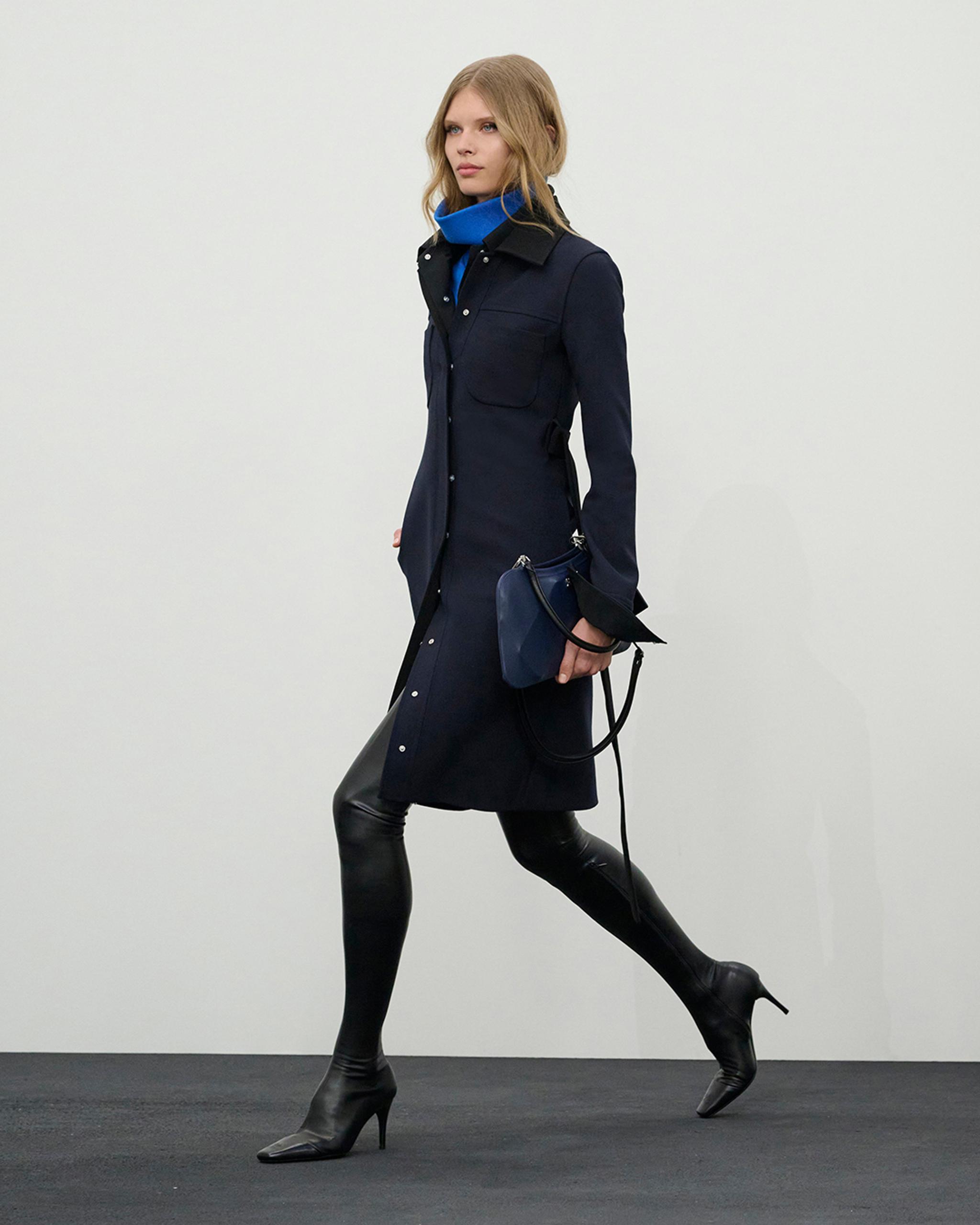 Elegant model in navy dress with blue accessories, showcasing Courrèges fashion on an e-commerce site.