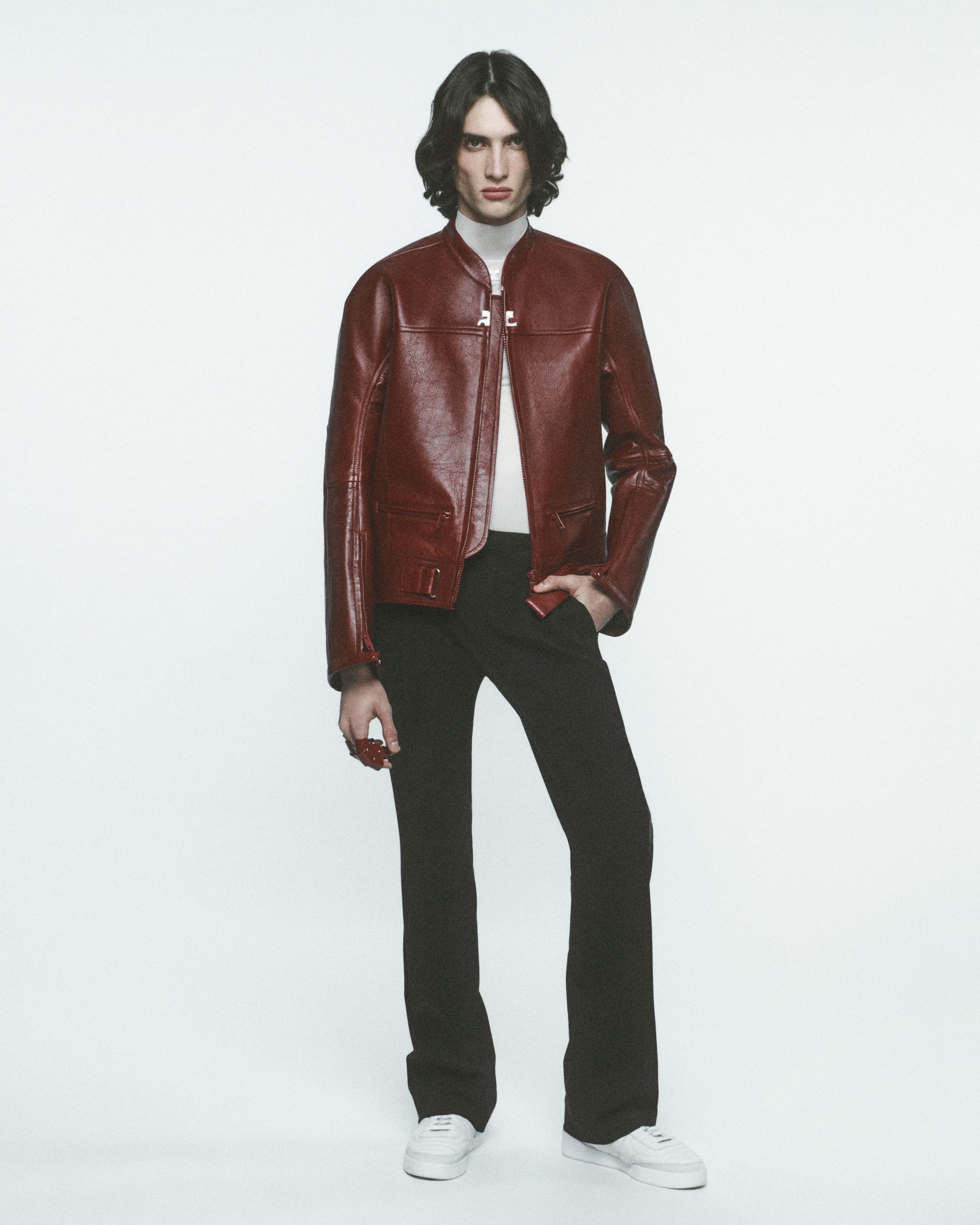 Modèle élégant portant une veste en cuir rouge, pantalon noir et baskets blanches sur fond blanc pour Courrèges.