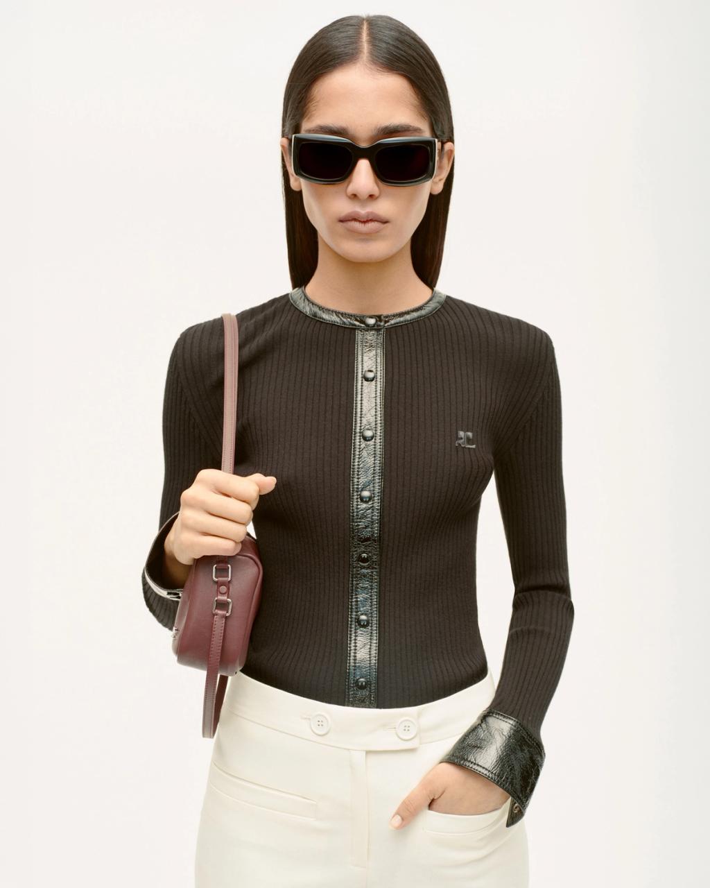 Elegant woman wearing black sunglasses, black top, and carrying a pink bag, model for Courrèges.