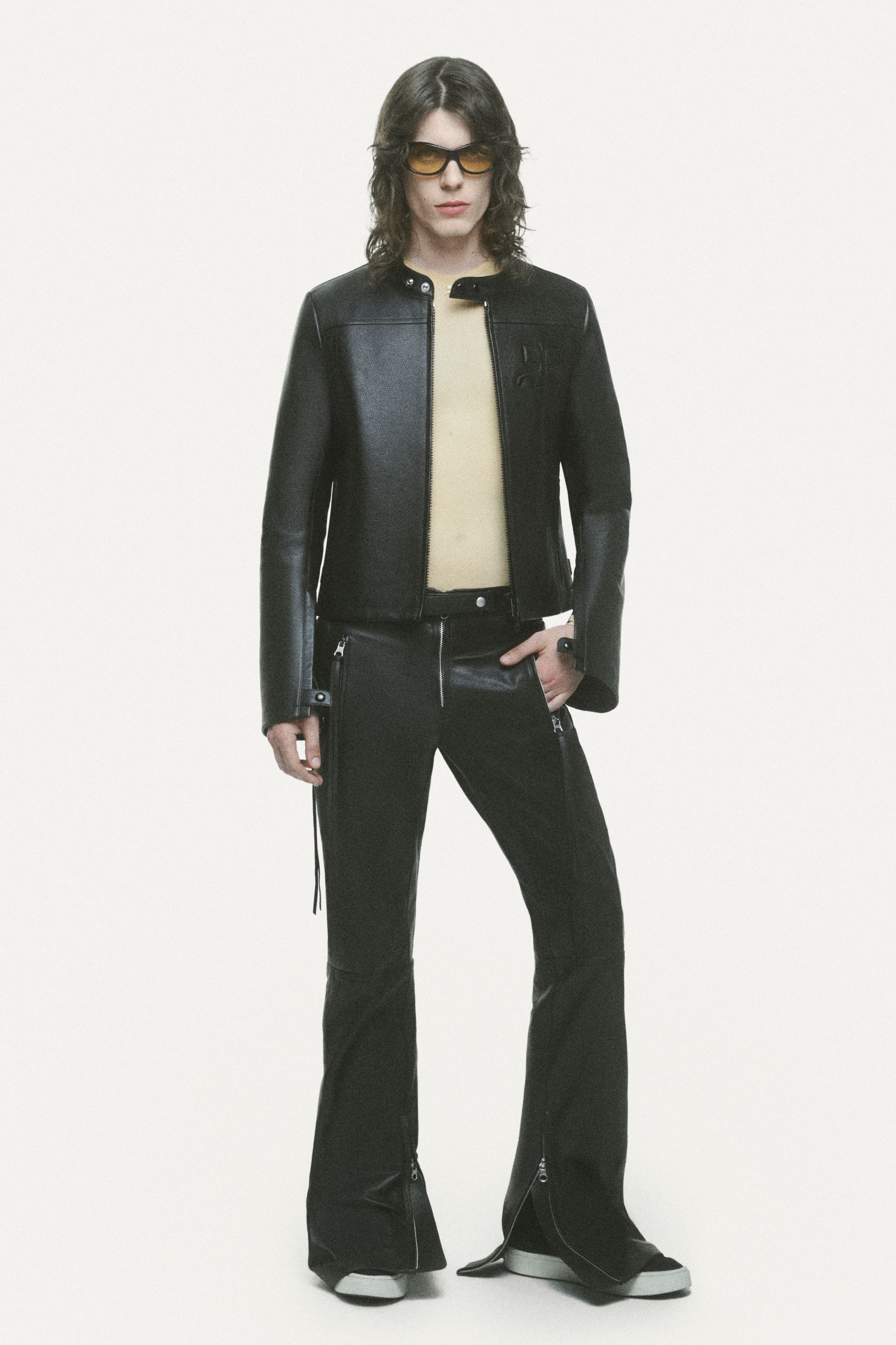 Elegant Courrèges model in black leather jacket, beige top, and trendy black pants with zippers.