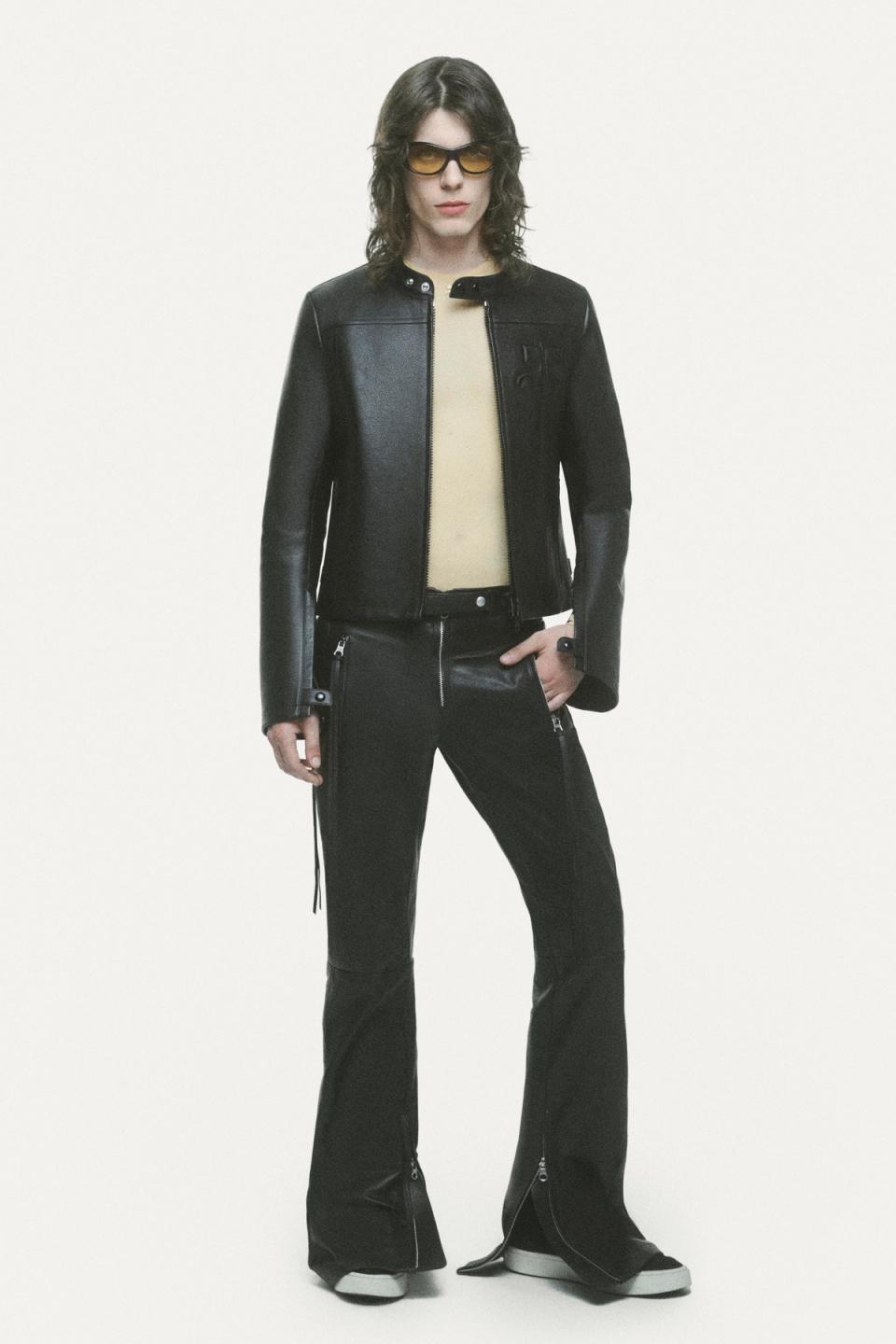 Elegant Courrèges model in black leather jacket, beige top, and trendy black pants with zippers.