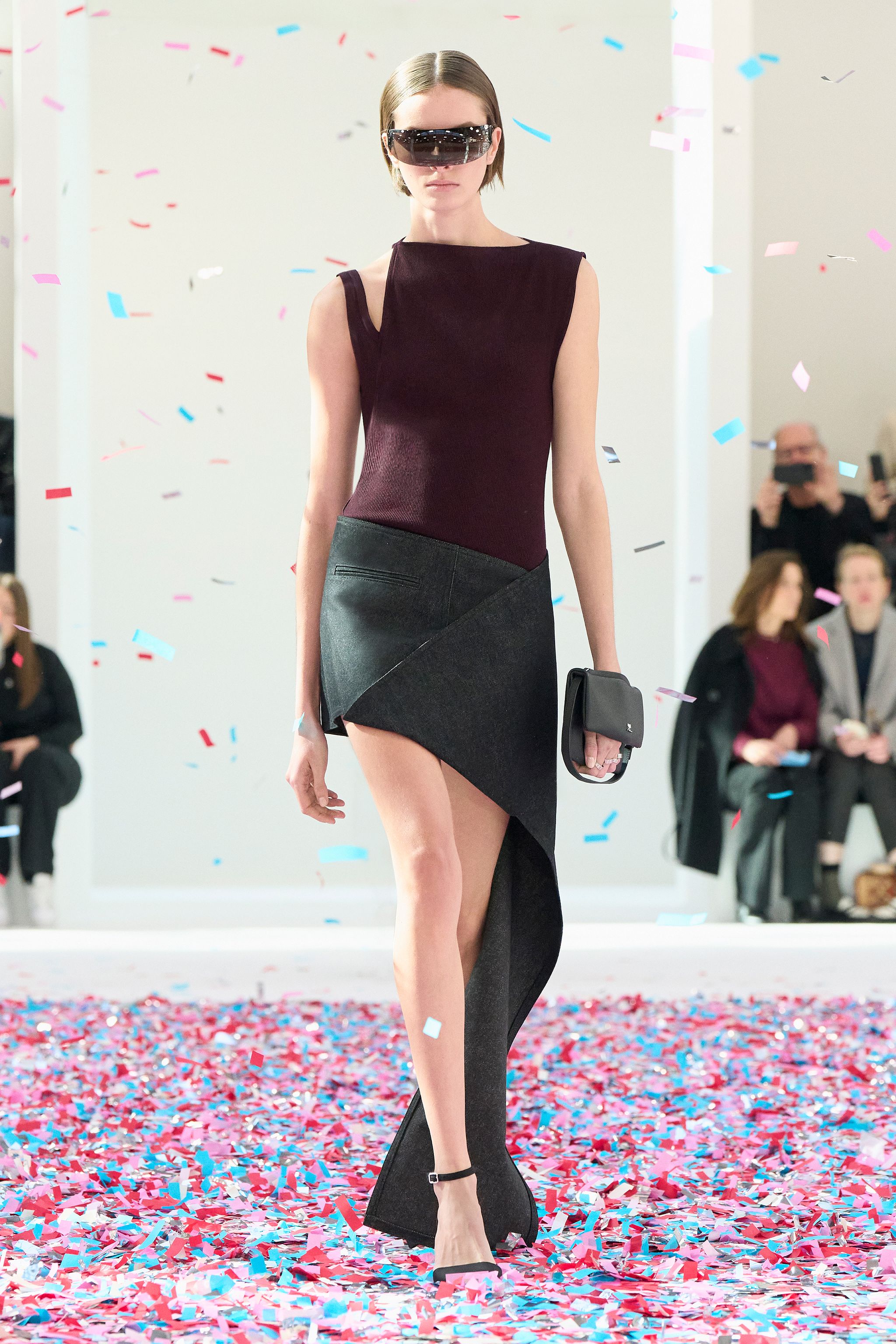 Elegant fashion runway model in Courrèges outfit with sunglasses, walking through colorful confetti.