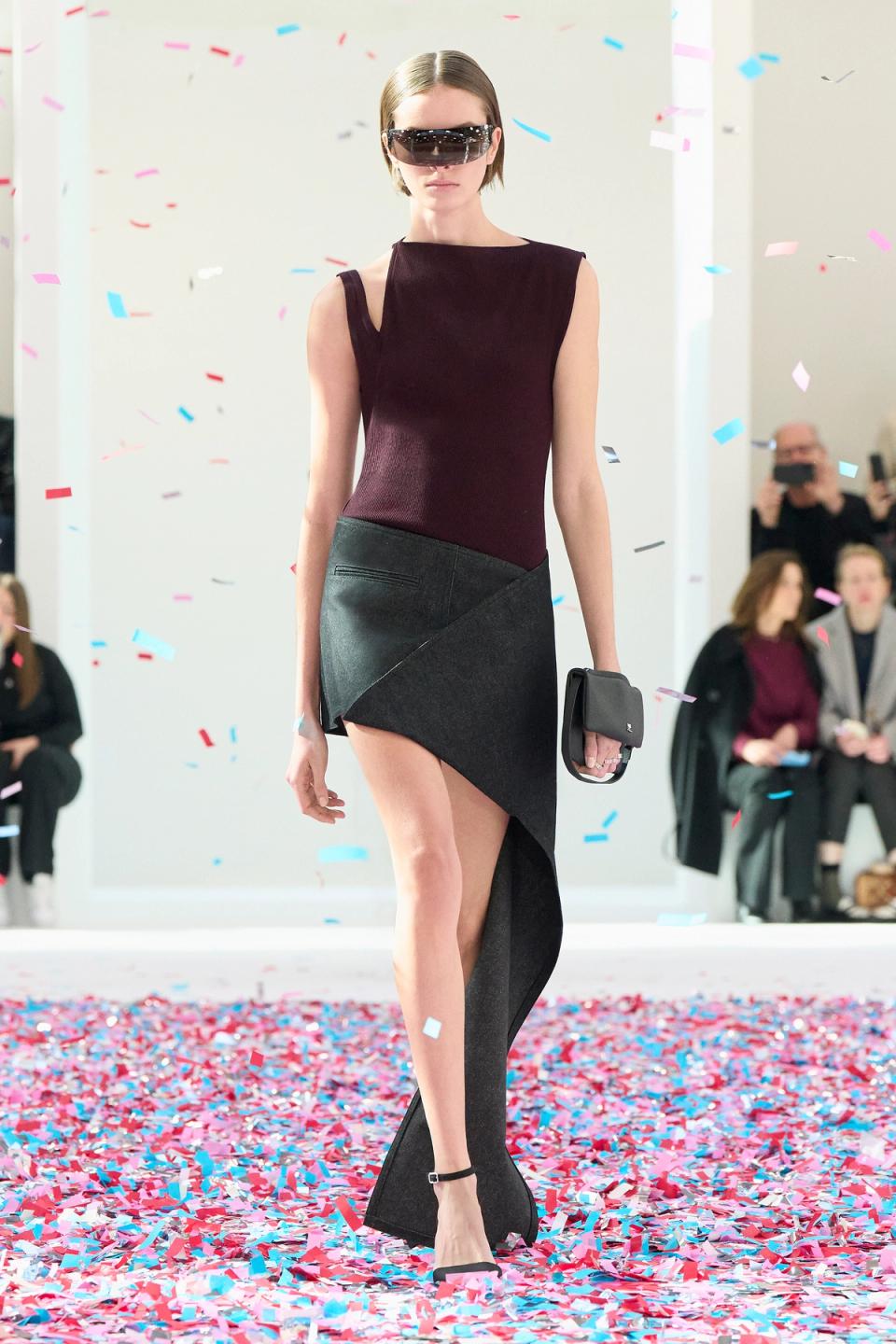 Elegant fashion runway model in Courrèges outfit with sunglasses, walking through colorful confetti.