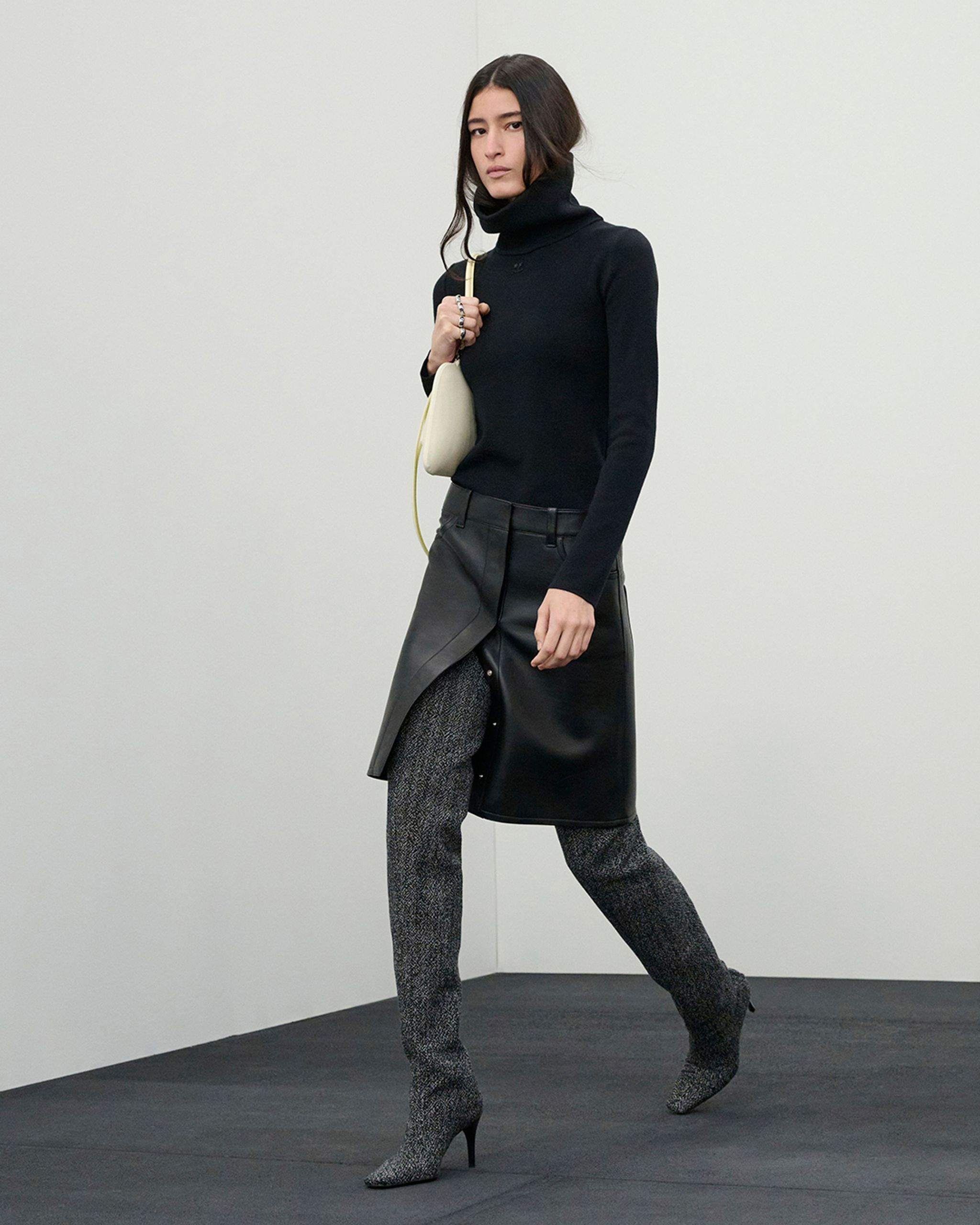 Pull noir à col roulé avec jupe en cuir embossed et talons pointus, style Courrèges.